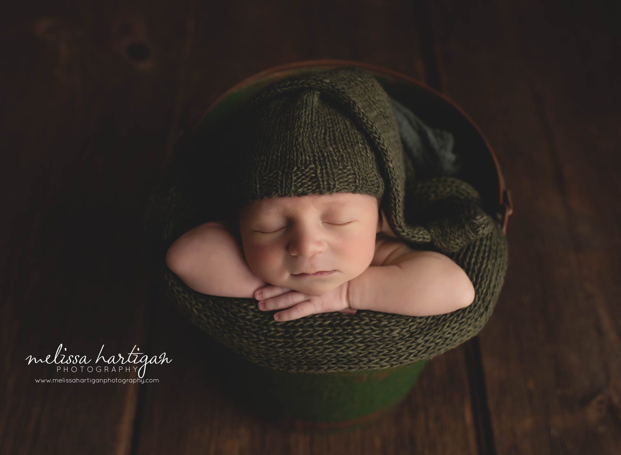 newborn boy posed in bucket with green knitted sleepy cap