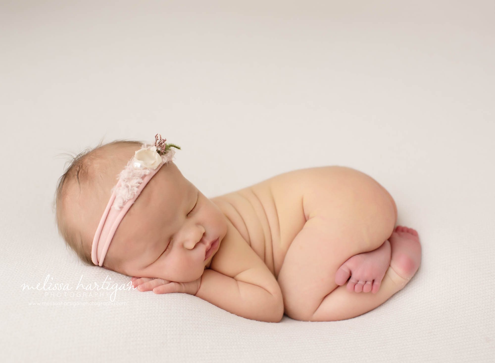 Baby girl posed on tummy with hand under cheek pink flower headband