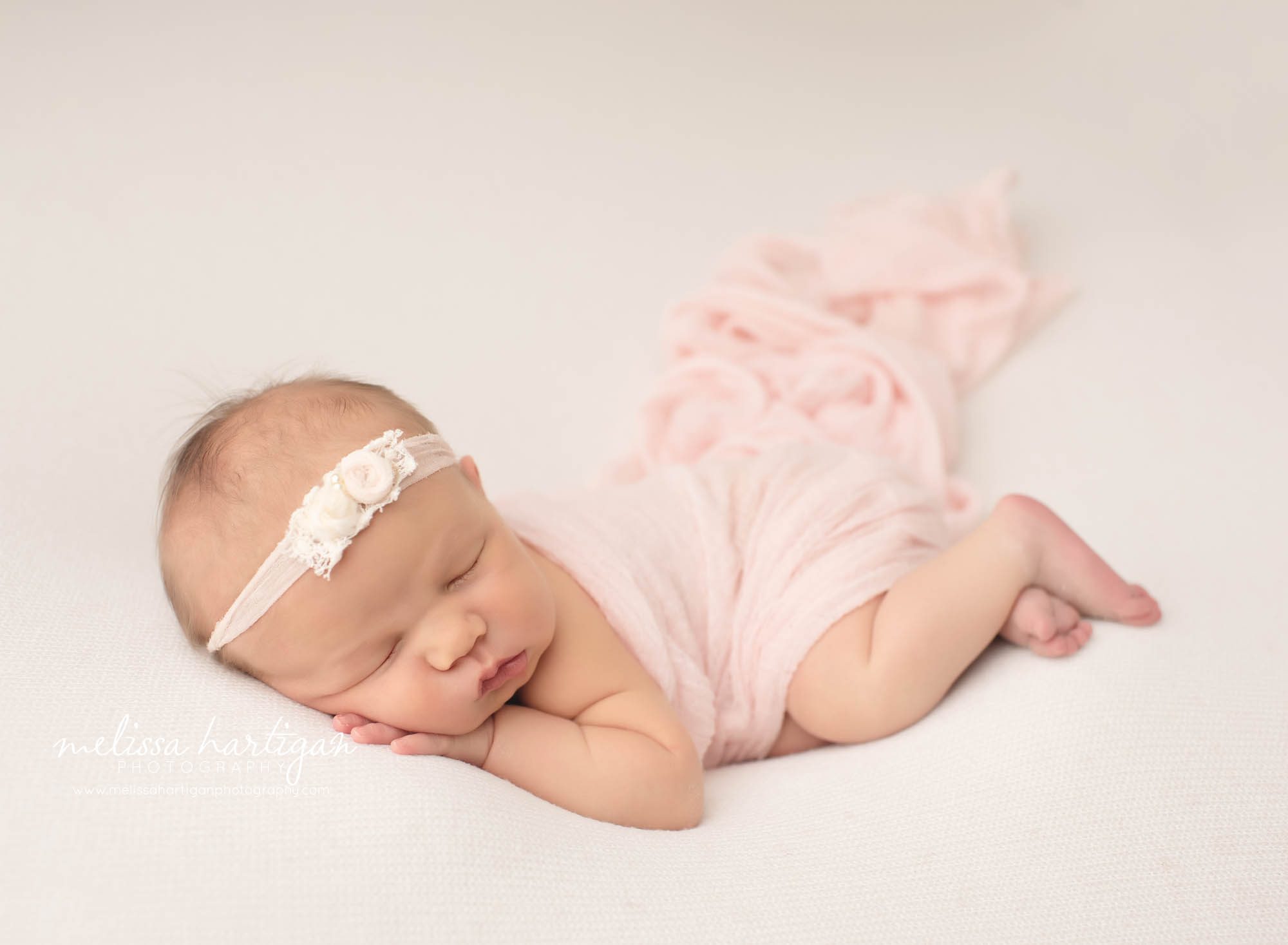 Baby girl posed on light backdrop with baby pink wrap and flower headband