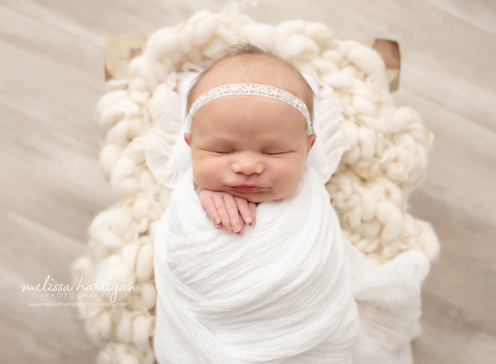 Baby girl smiling in white wrap laying on cream colored textured layer