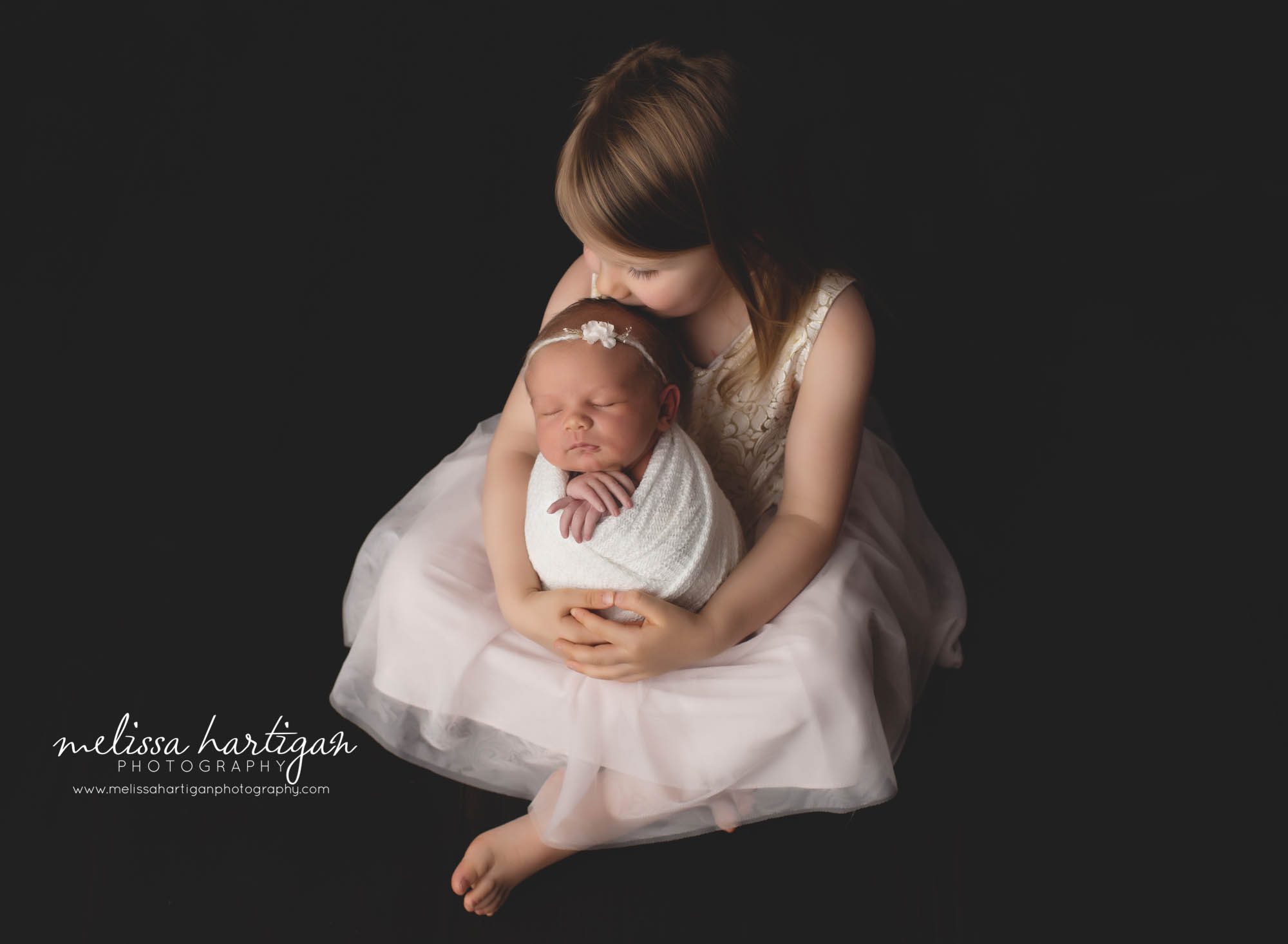 Older sister kidding baby sisters head studio newborn photographer session sibling pose
