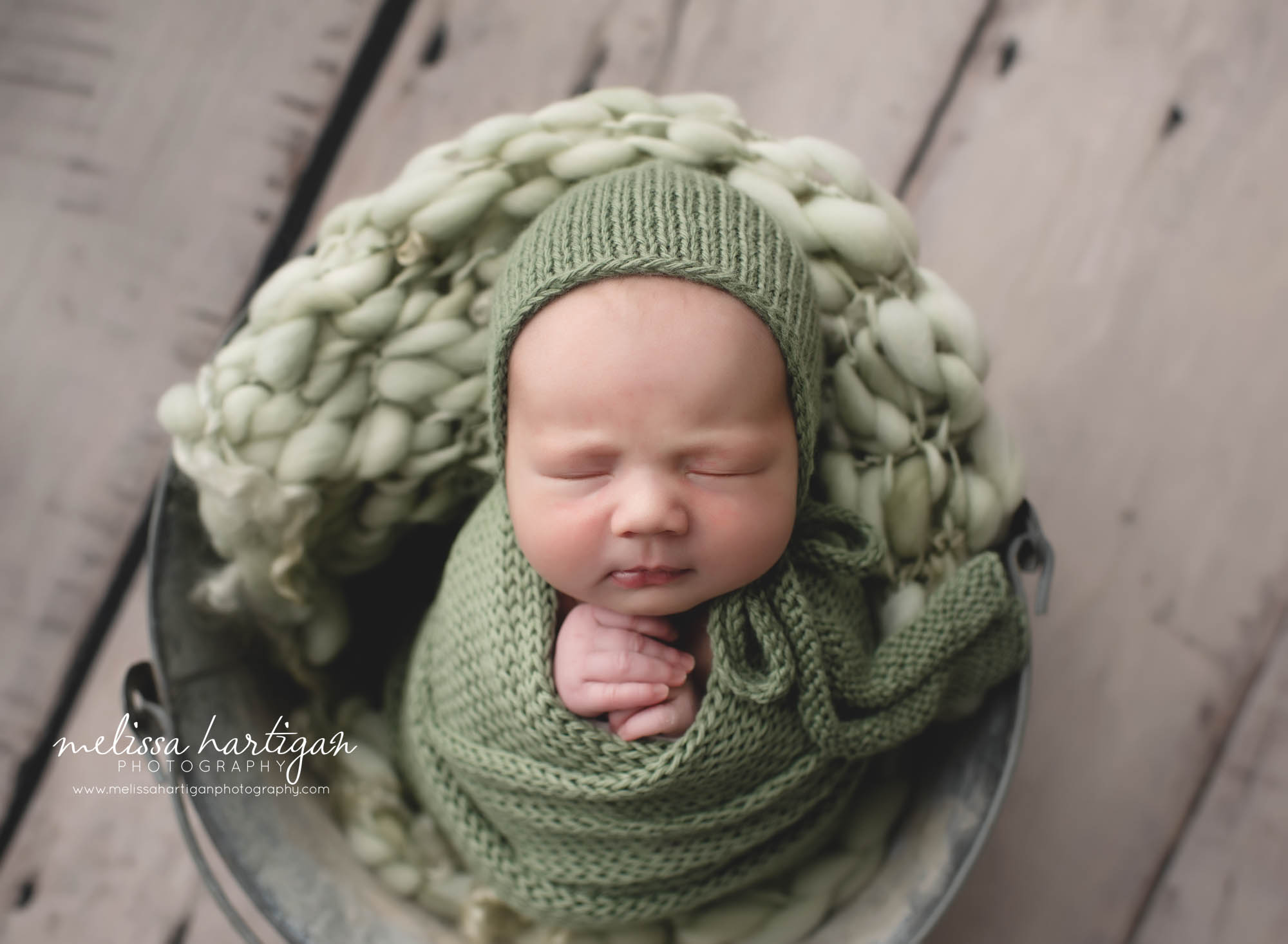 Baby girl pose din metal bucket with sgae green knitted layer wrap and matching bonnet CT baby photographer stafford