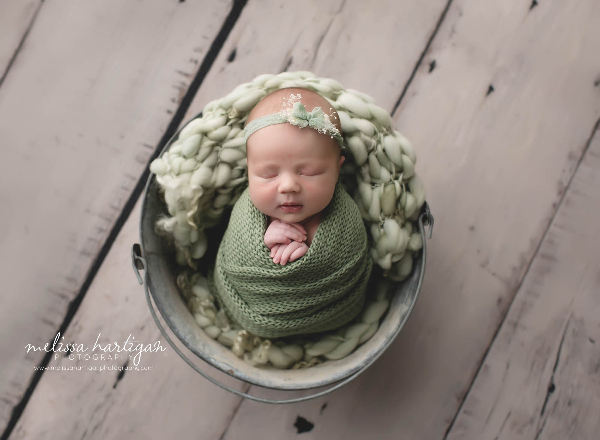 baby girl in bucket with green colored layer, wrap and headband
