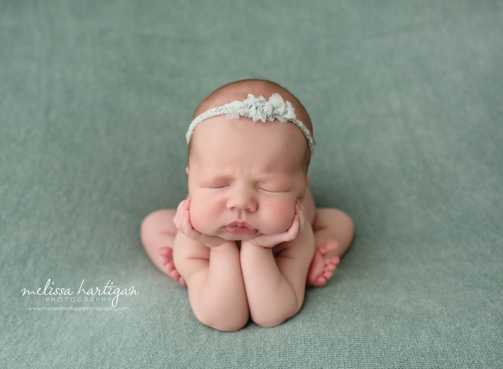 Baby girl posed in froggy pose with sage green backdrop