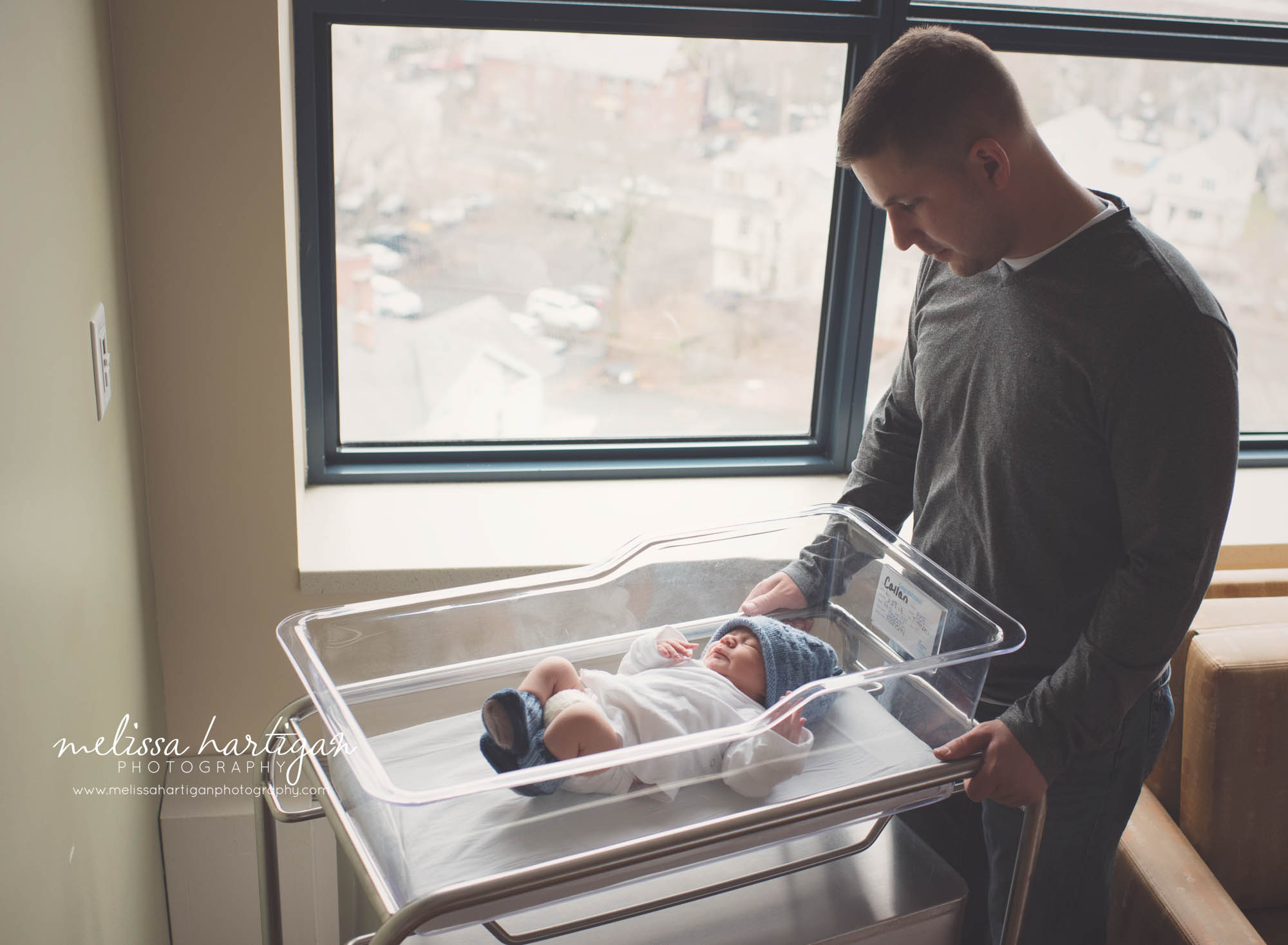 newborn baby is hospital basinet with dad standing over looking at his new baby