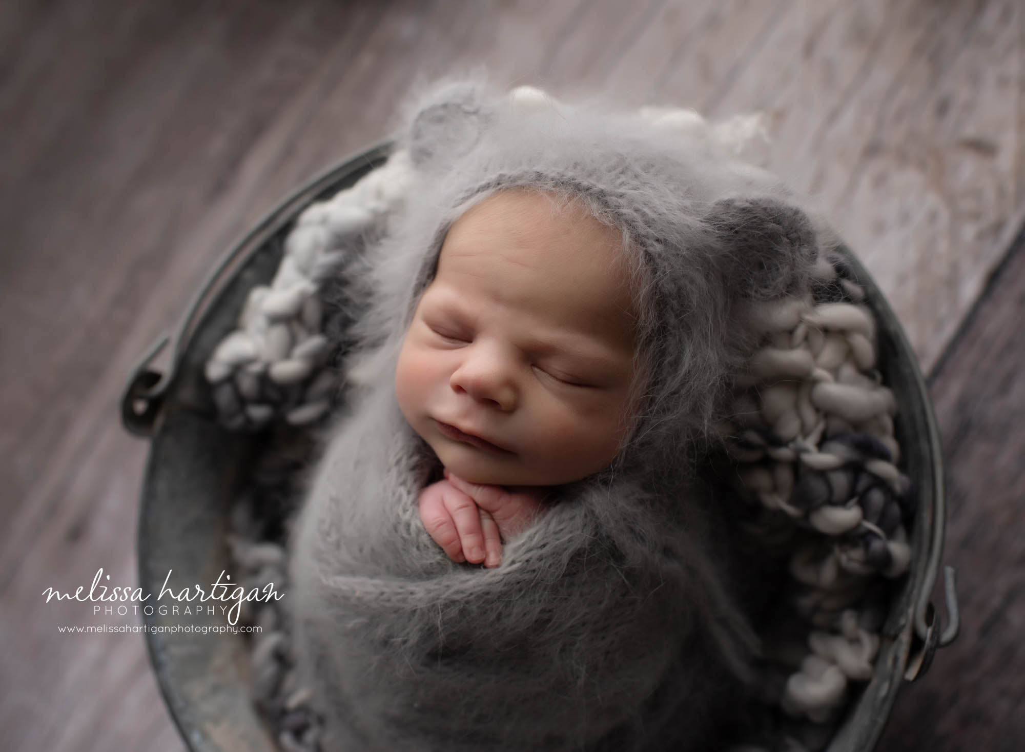baby boy posed in metal bucket with gray knitted bear hat on and gray knitted wrap newborn photography ct