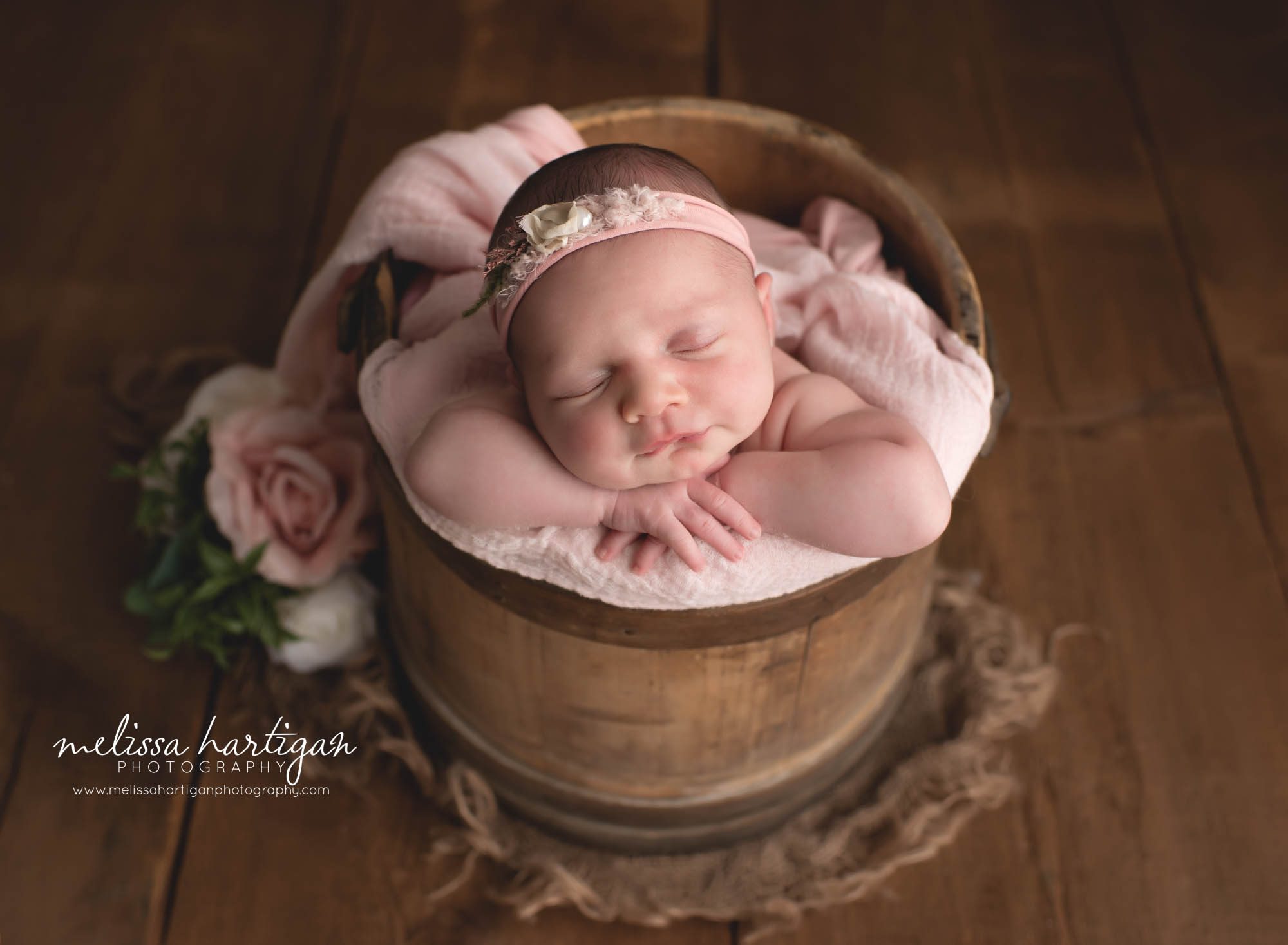 Baby girl posed in wooden rustic busket with pink flowers and pink headband