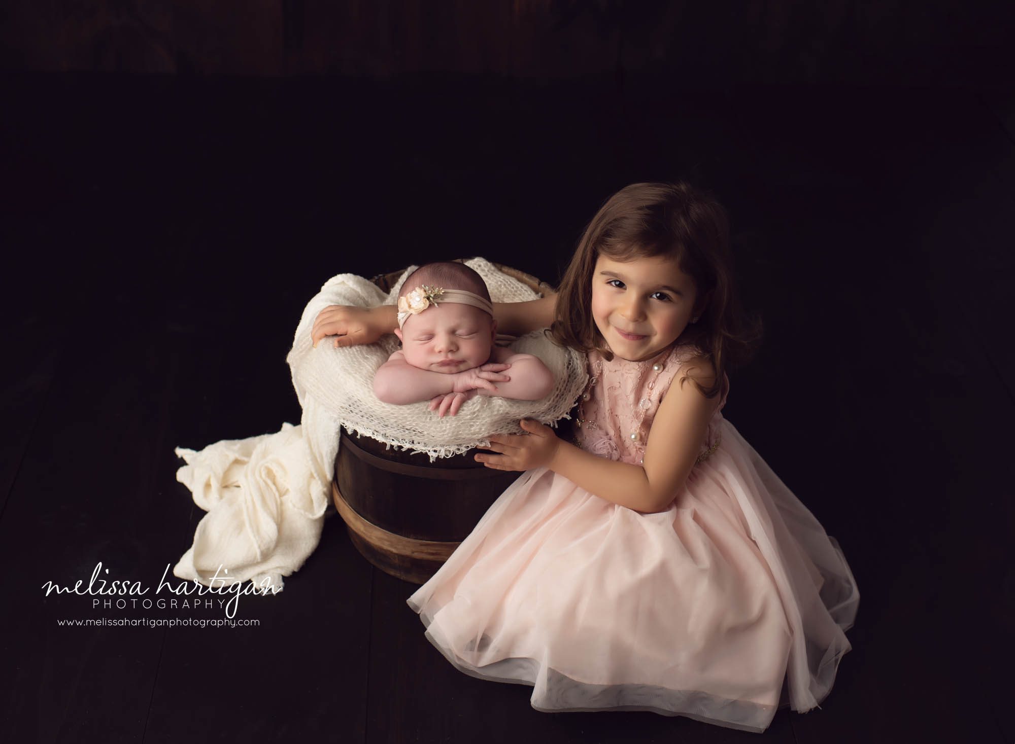 Baby girl posed in bucket with older sister sitting beside her