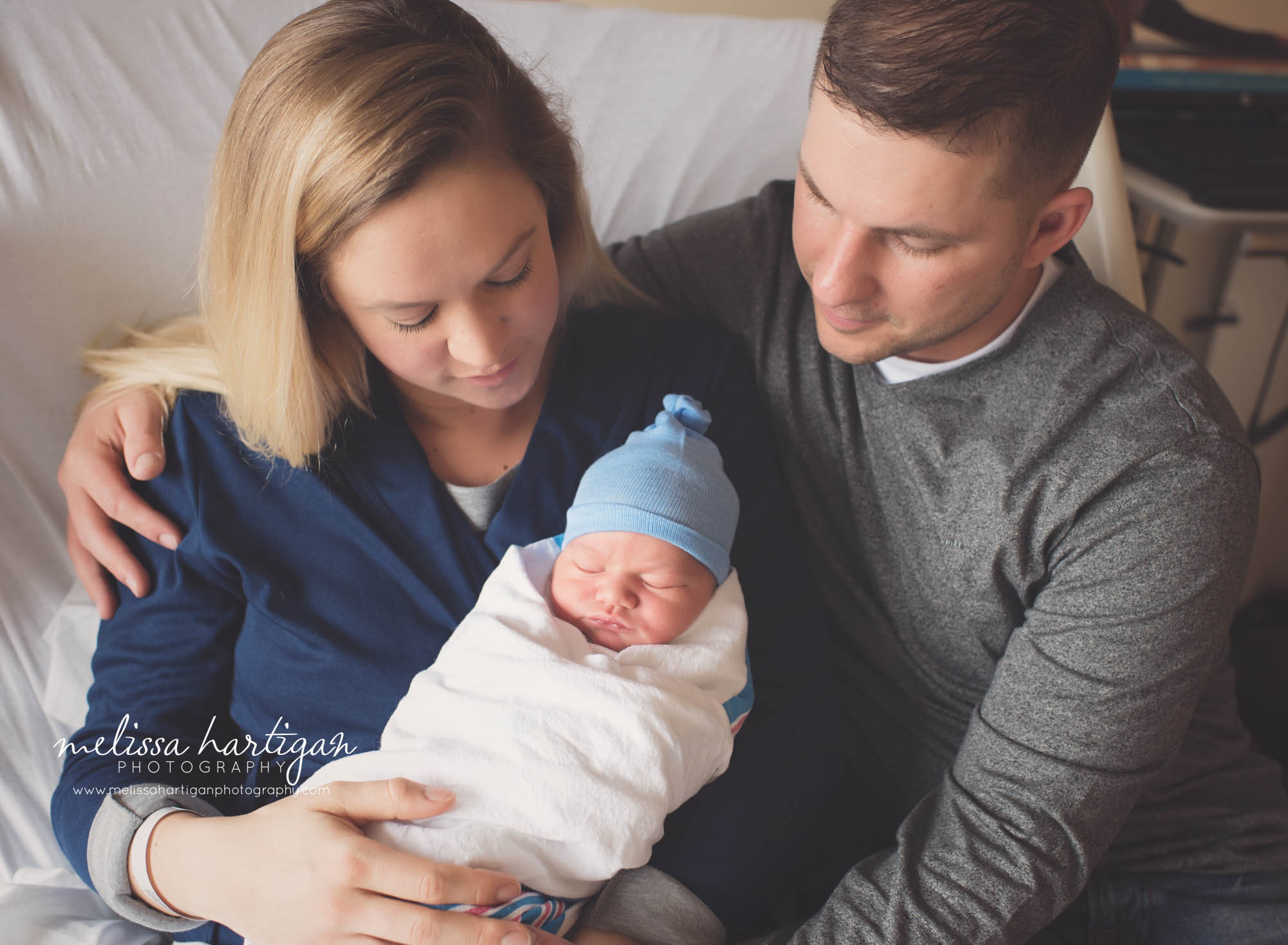 new parents holding their baby boy sitting on hospital bed
