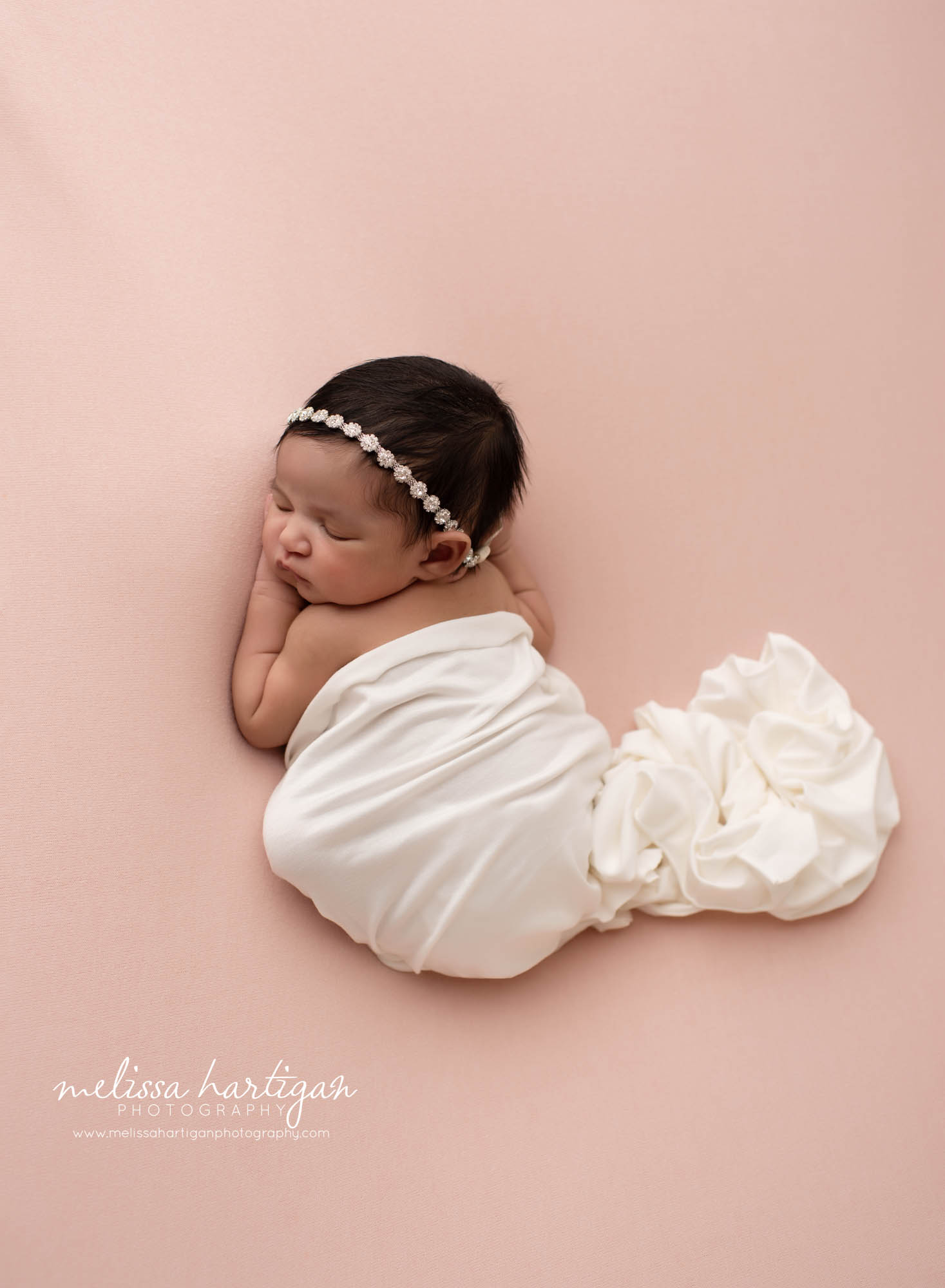 baby girl posed on tummy with white wrap wearing jeweled headband