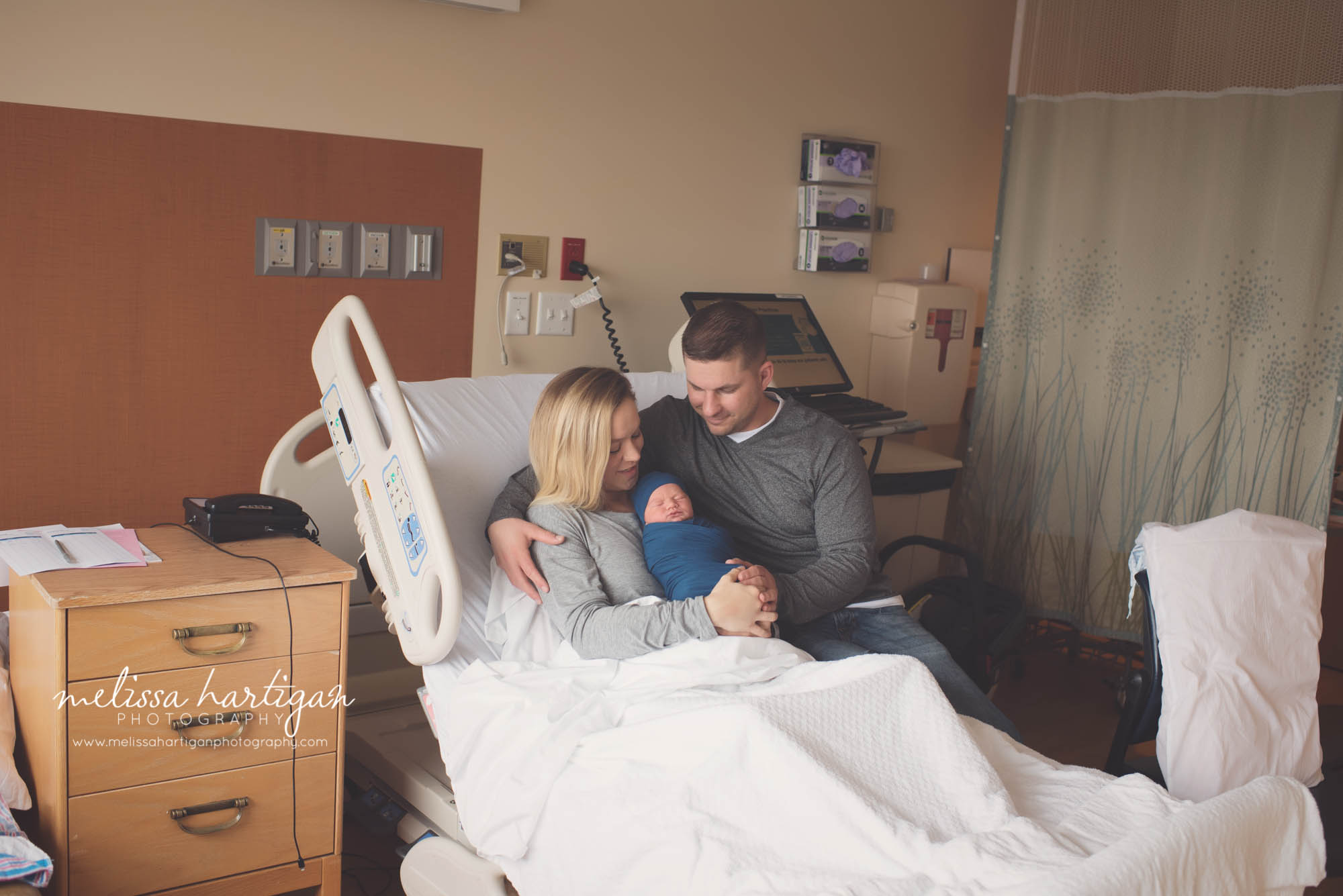mom holding her swaddled baby boy with dad sitting next to them a family moment in the hospital CT newborn photographer