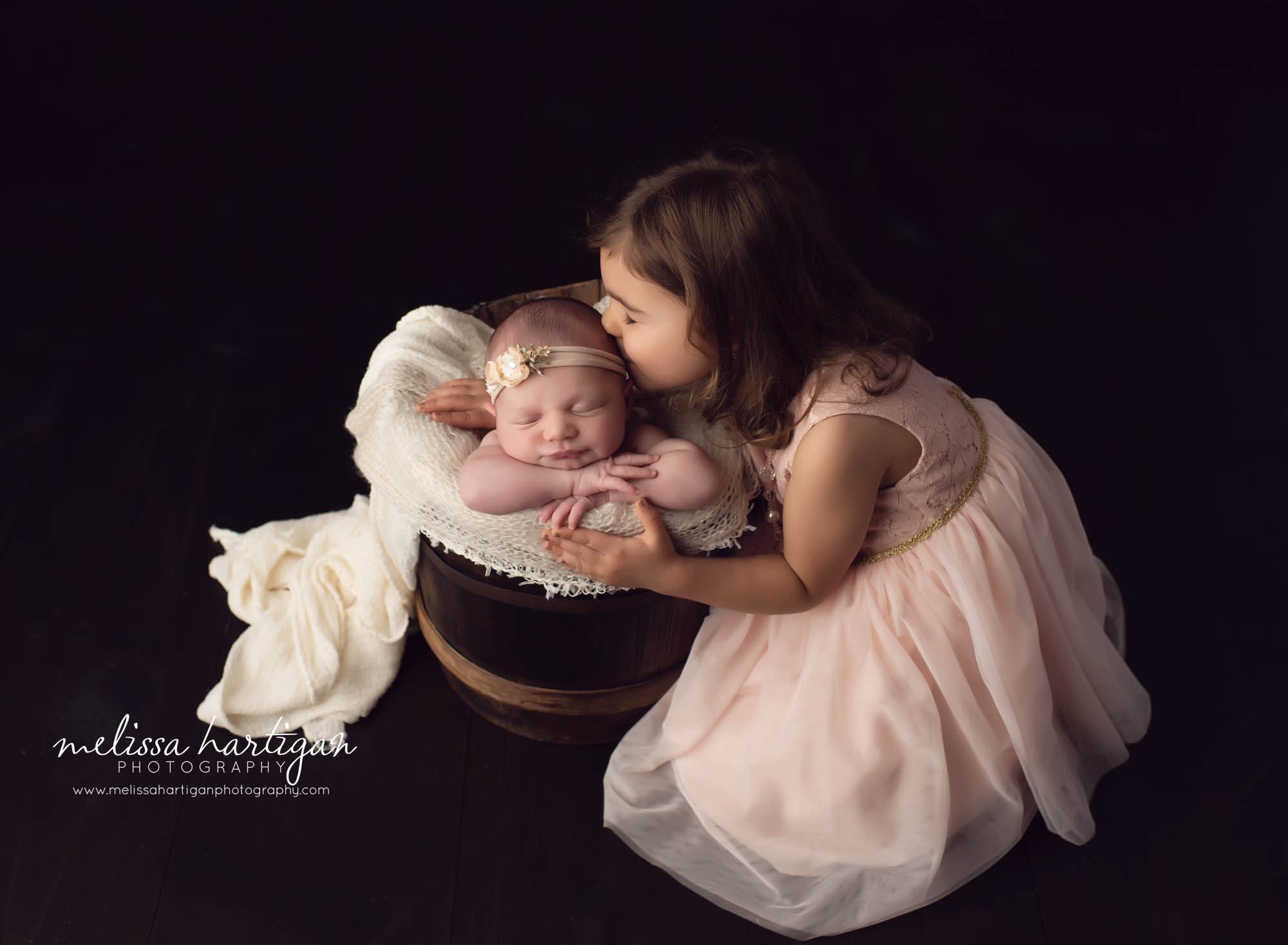big sister giving baby sister a kid on the head baby girl posed in wooden bucket