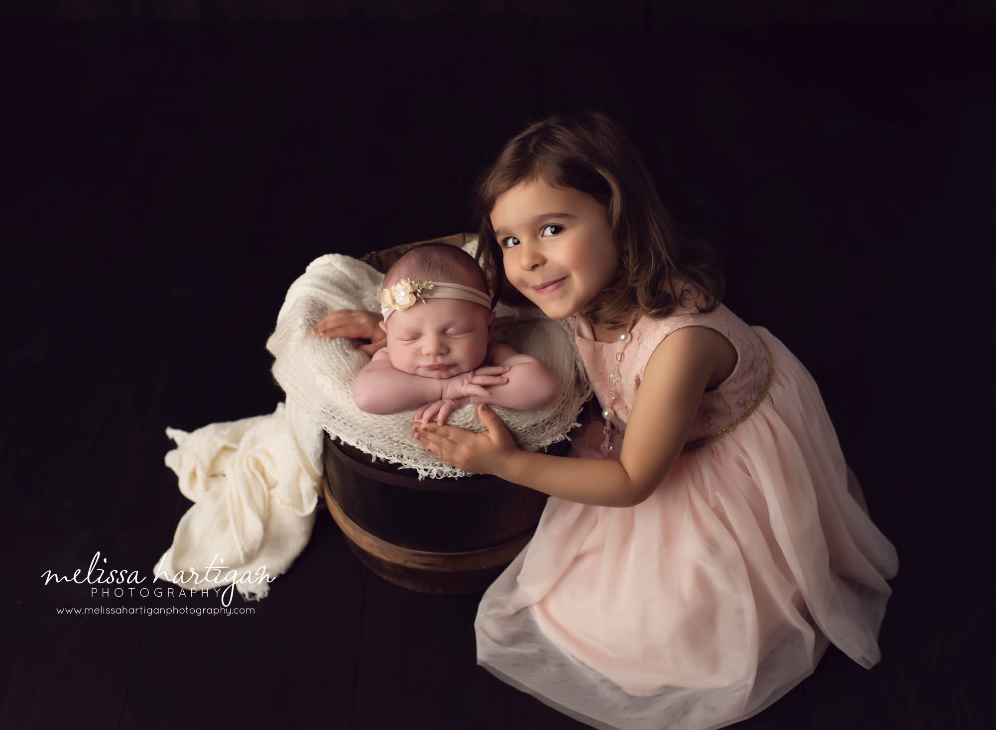 baby girl posed in bucket with big sister leaning next to her