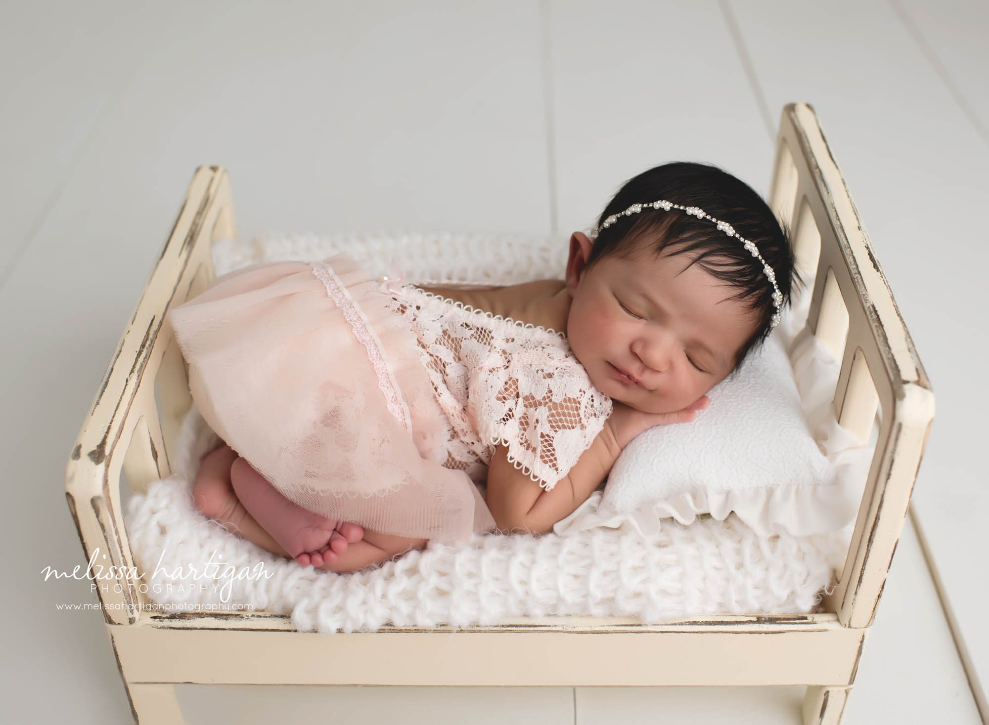 baby girl posed on wooden bed prop with white lace and pink outfit