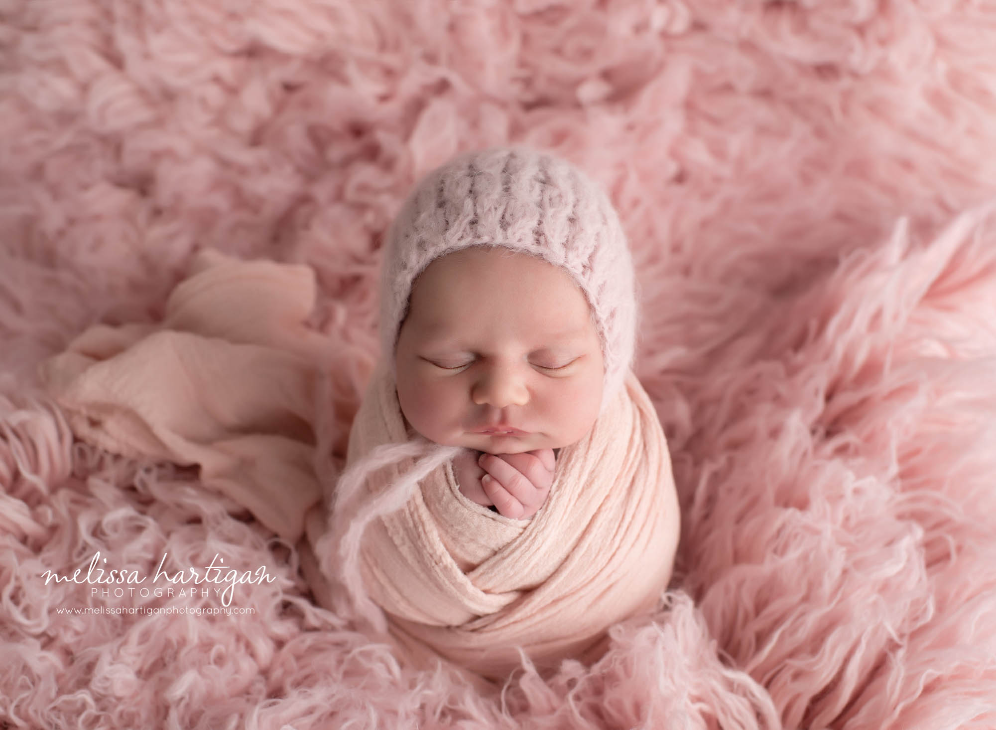 Baby girl wrapped on flokati rug with light pink bonnet