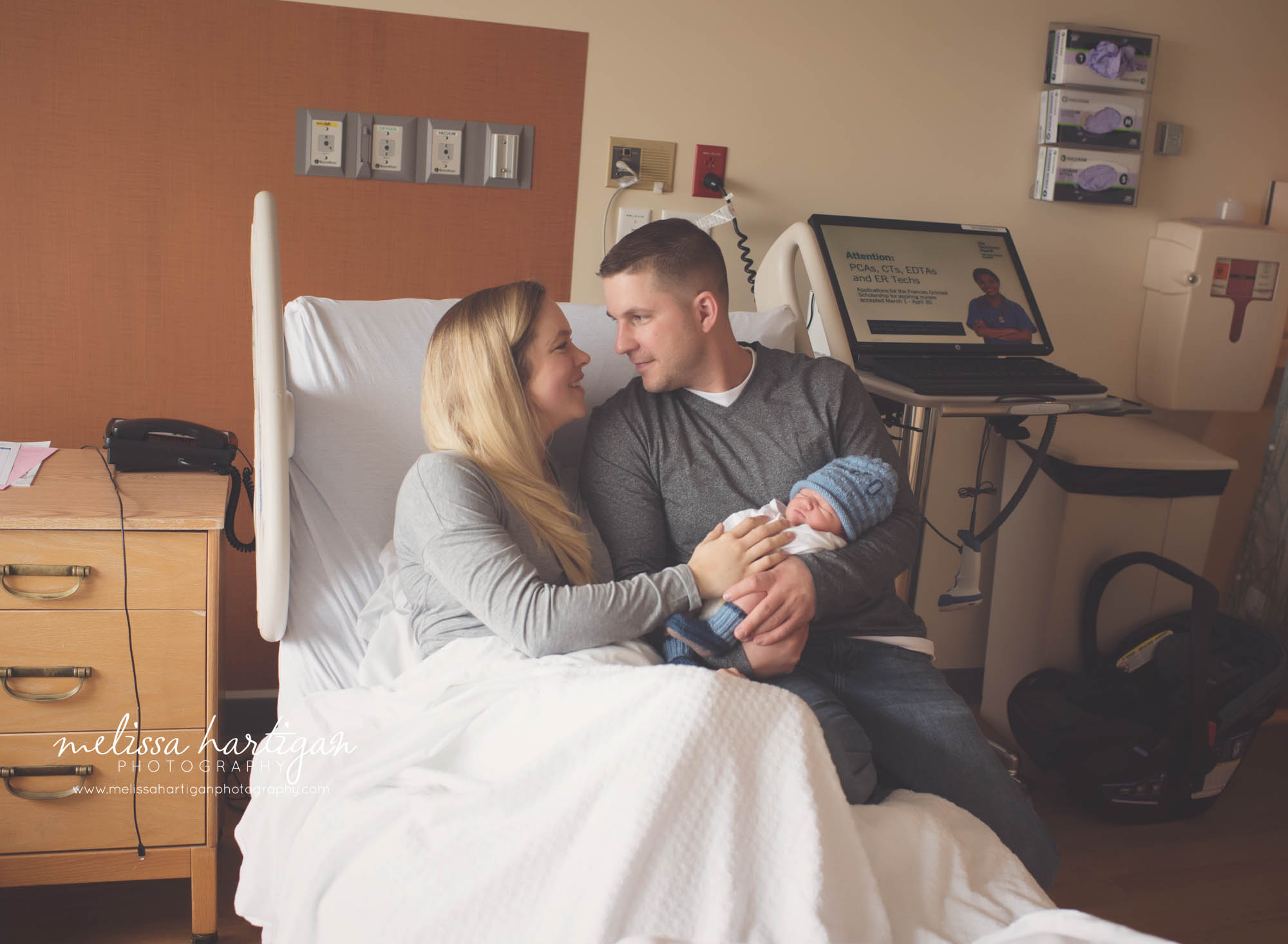 dad holding his baby boy with mom sitting in the hospital bed