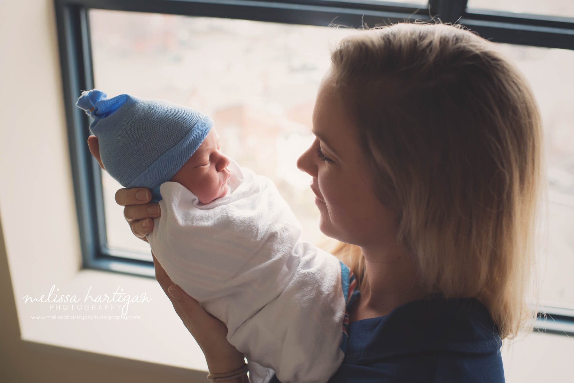 mom holding her newborn baby boy in hospital room by hospital window