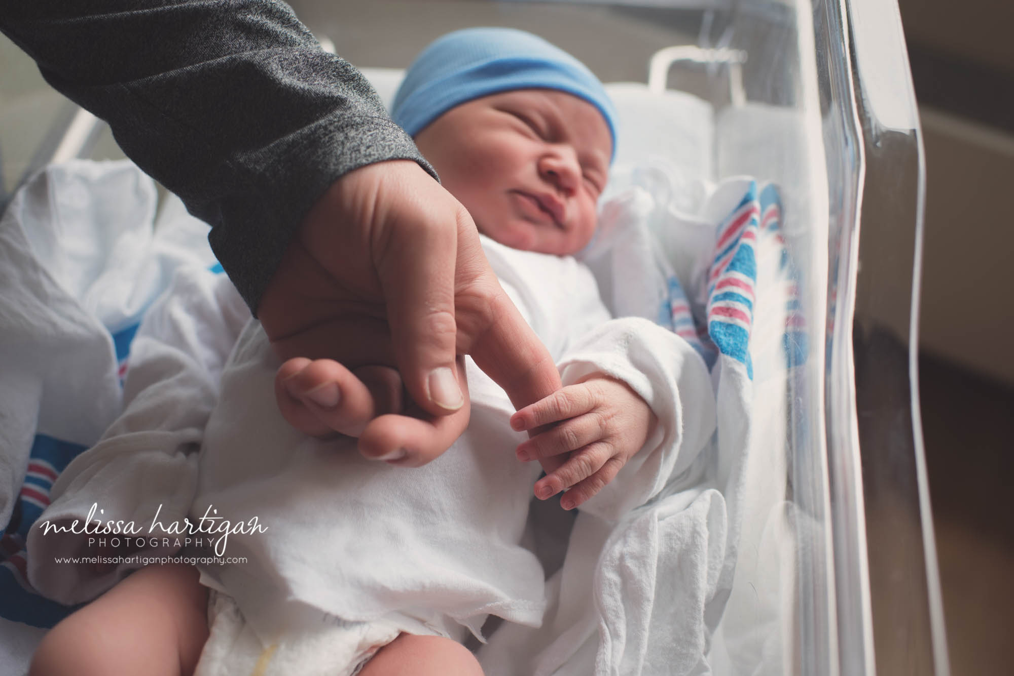 newborn baby boy laying in hospital bassinet holding dads finger