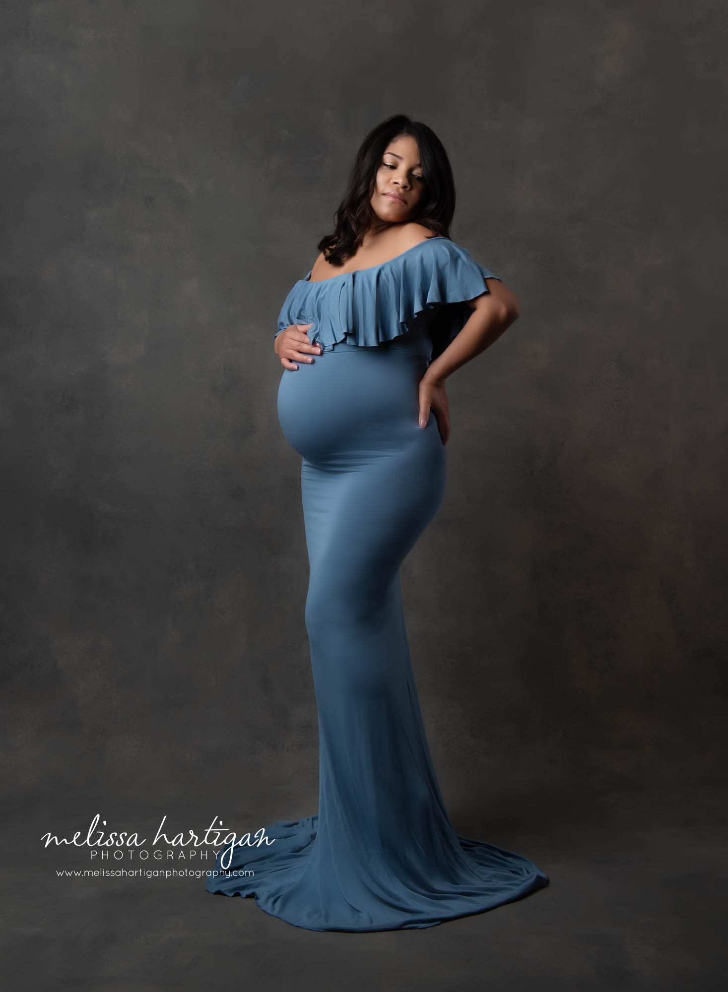 Mother to be standing in photography studio during maternity session mom wearing blue ruffled off the shoulder maternity dress