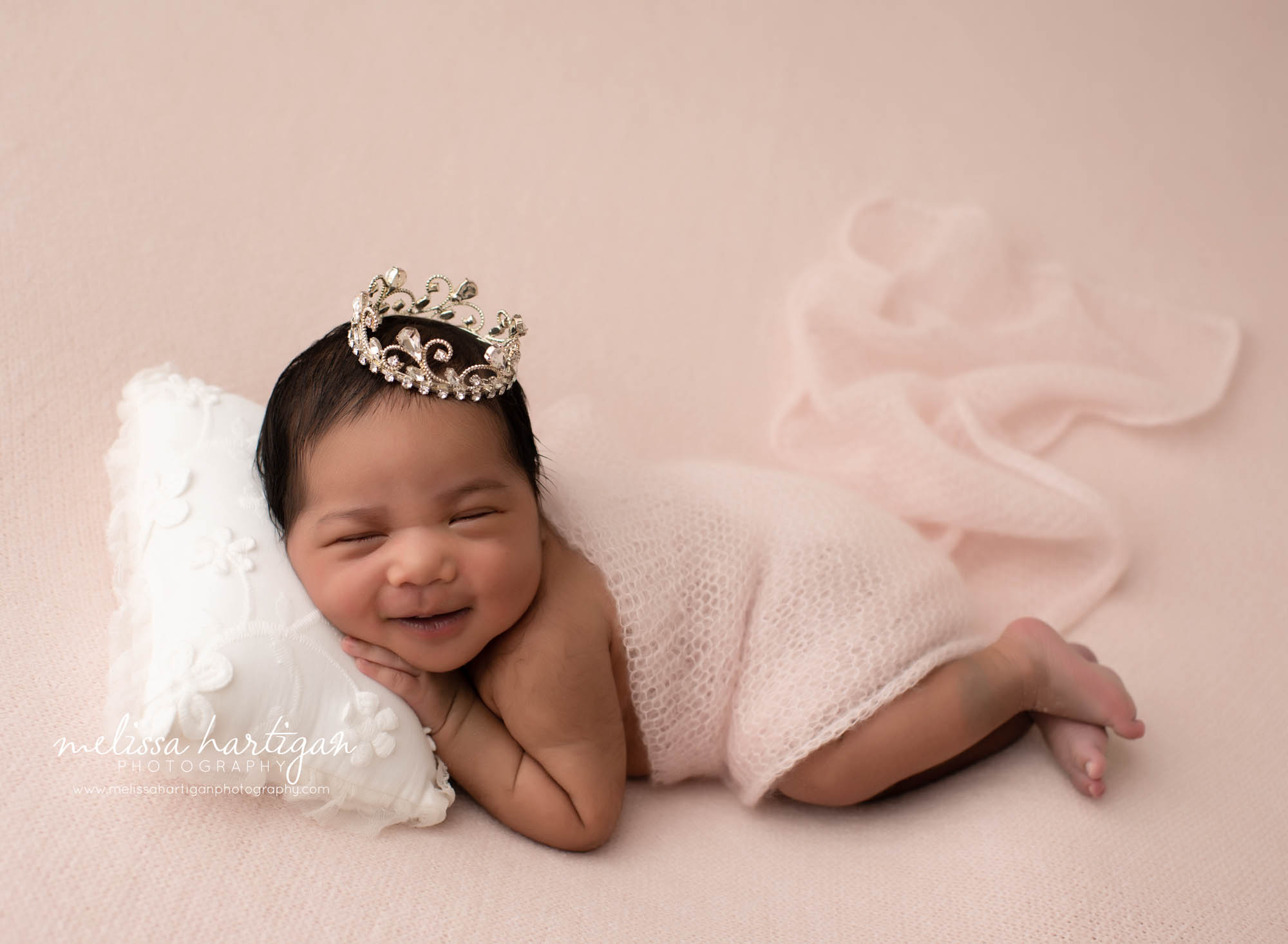 baby girl smiling posed on pink blanket with jeweled crown newborn pilow