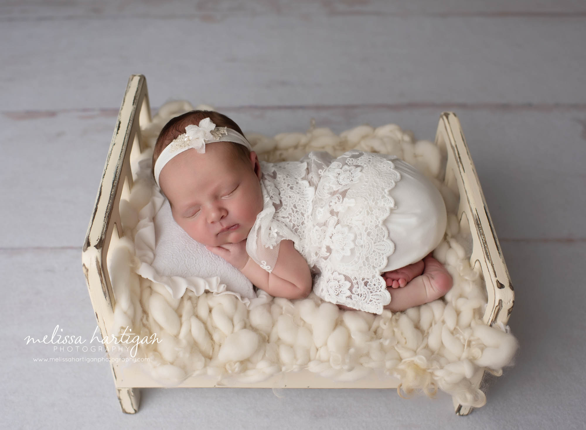 baby girl posed on tummy wearing lace outfit on cream colored wooden bed