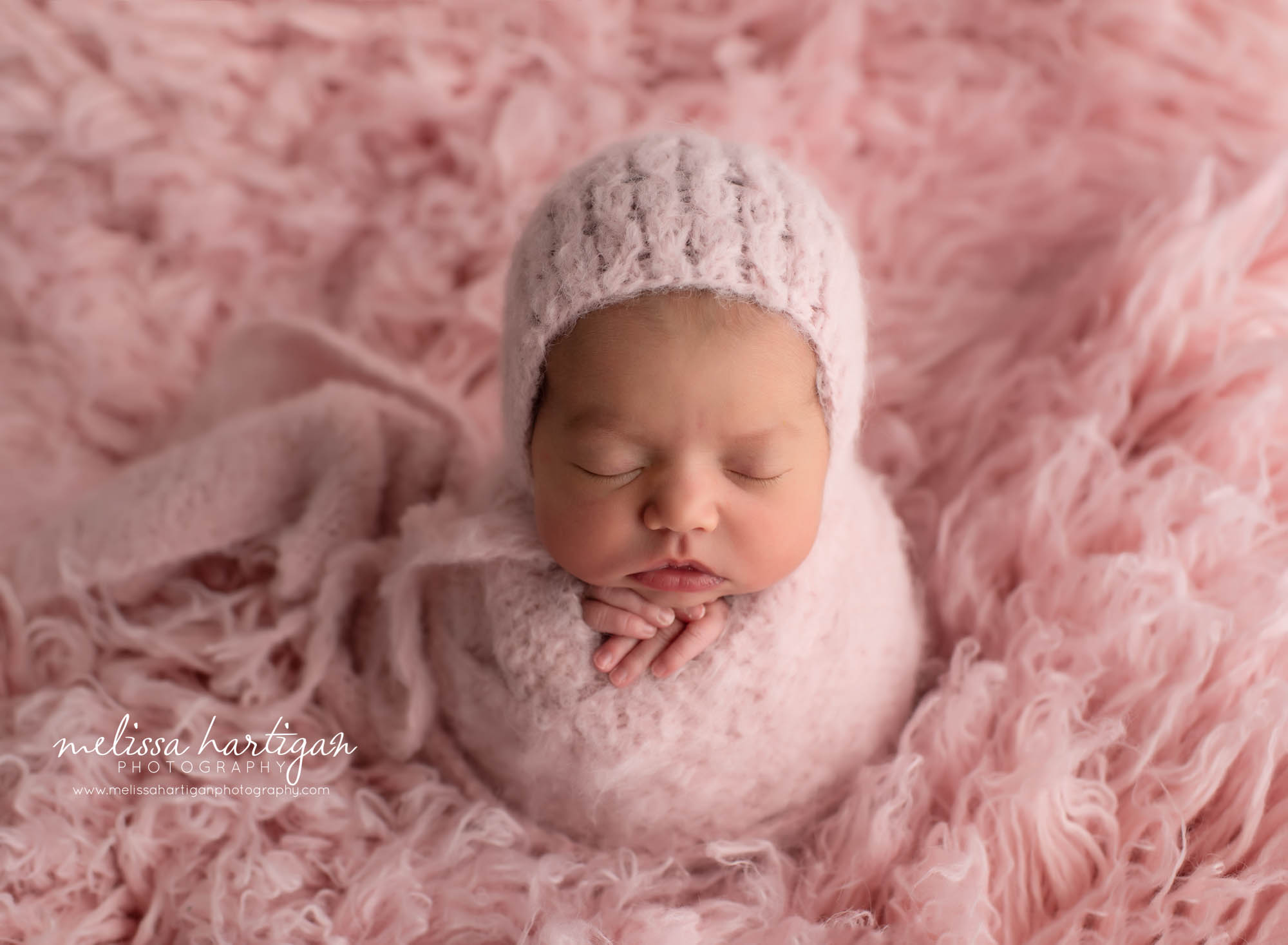 baby girl wrapped in pink knitted wrap posed on pink flokati rug with pink knitted bonnet ct newborn photography