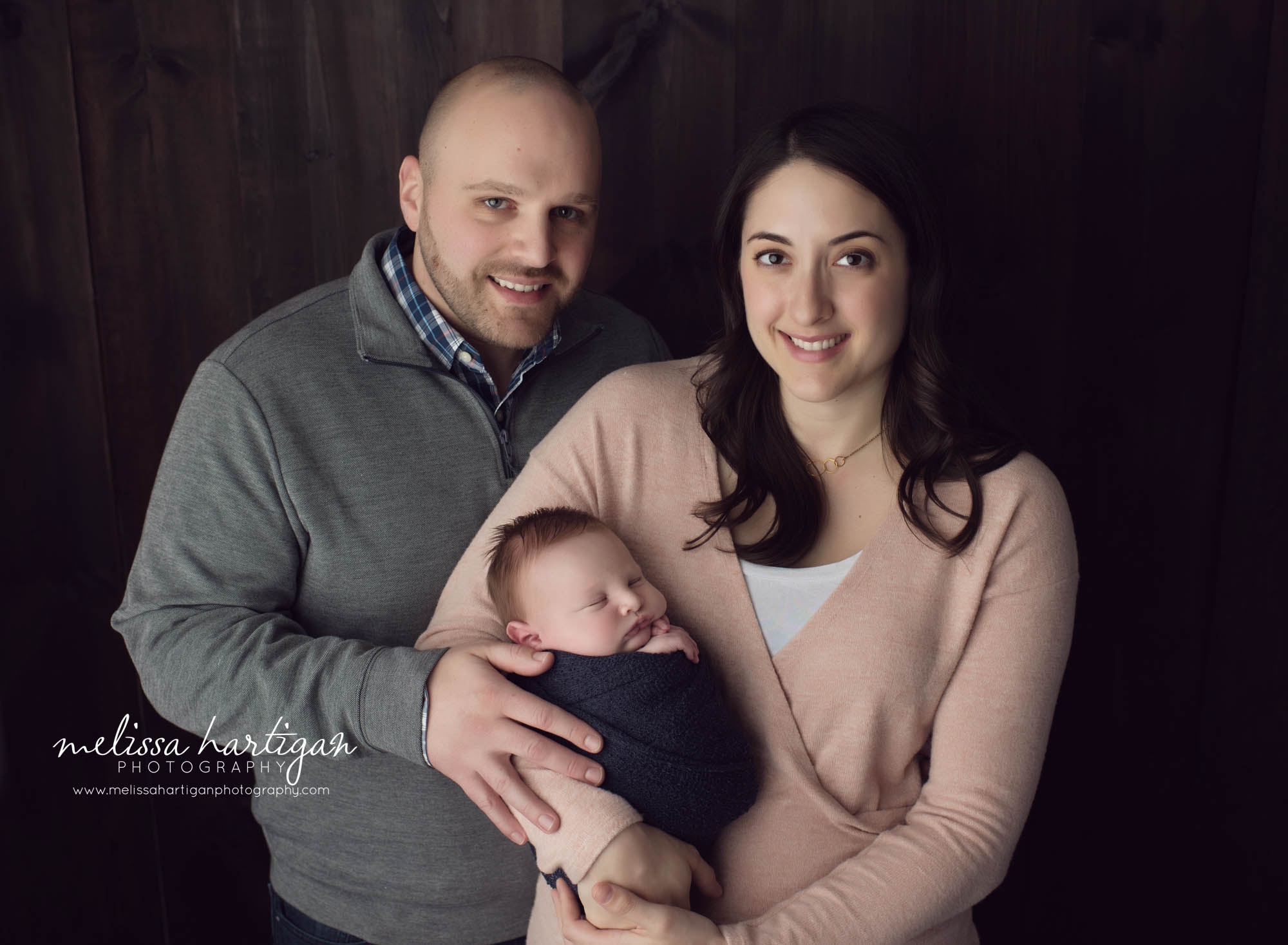mom dad and newborn baby studio standing family pose looking at camera