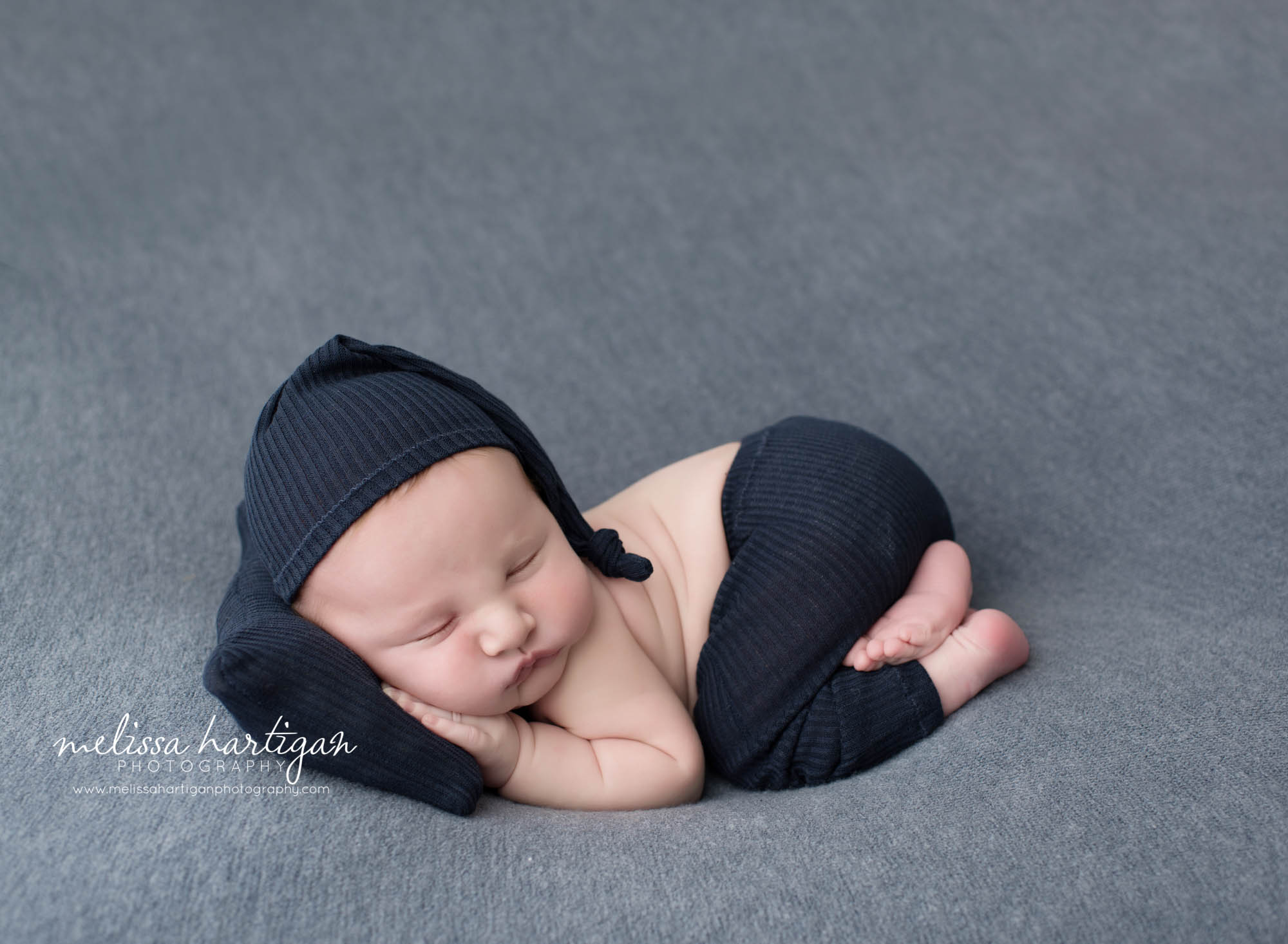 newborn baby boy posed on tummy with head on newborn pillow wearing dark blue hat and pants set West Suffield CT Newborn Photography