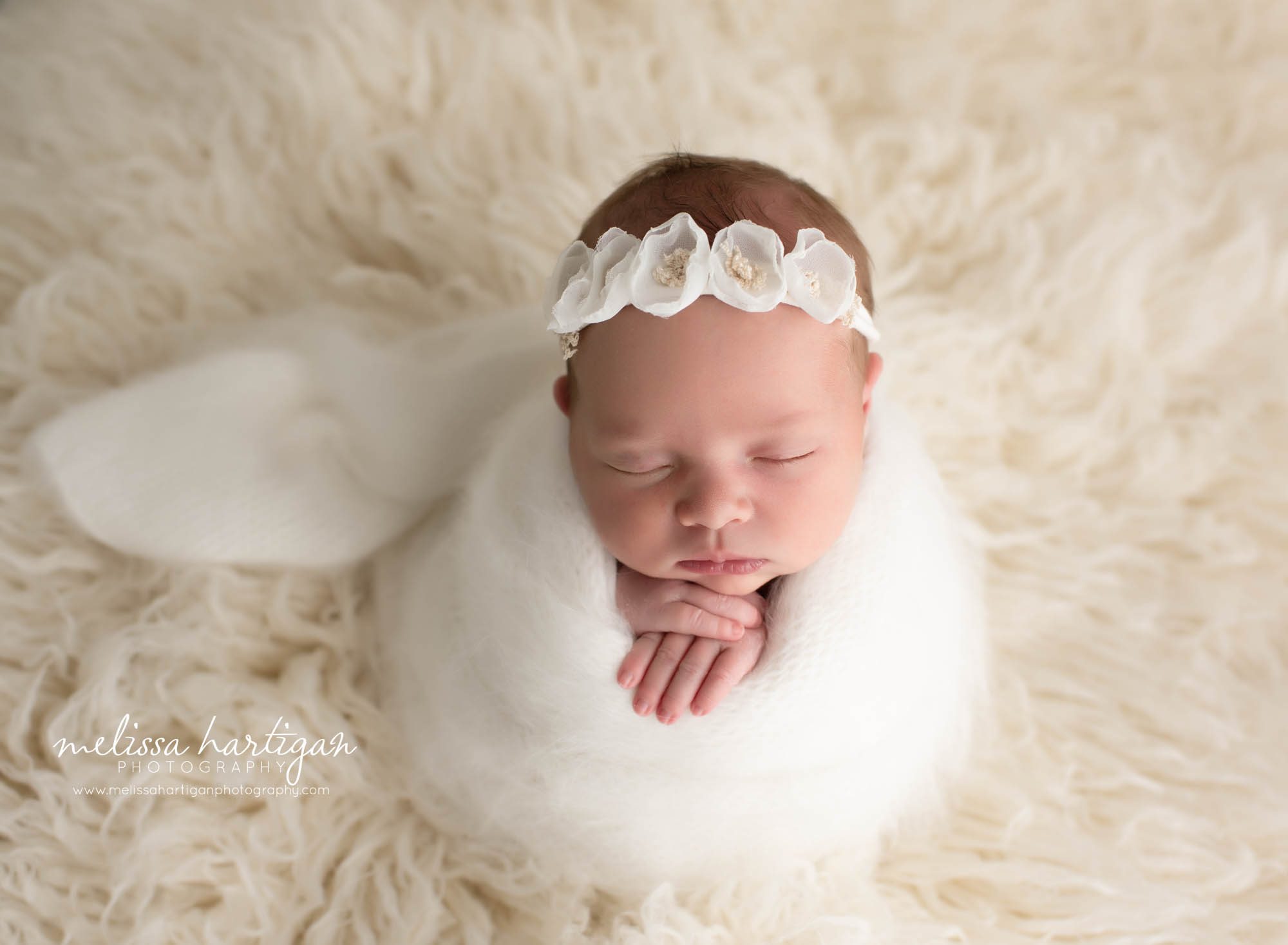 baby girl wrapped in white knitted wrap on flokati with flower headband