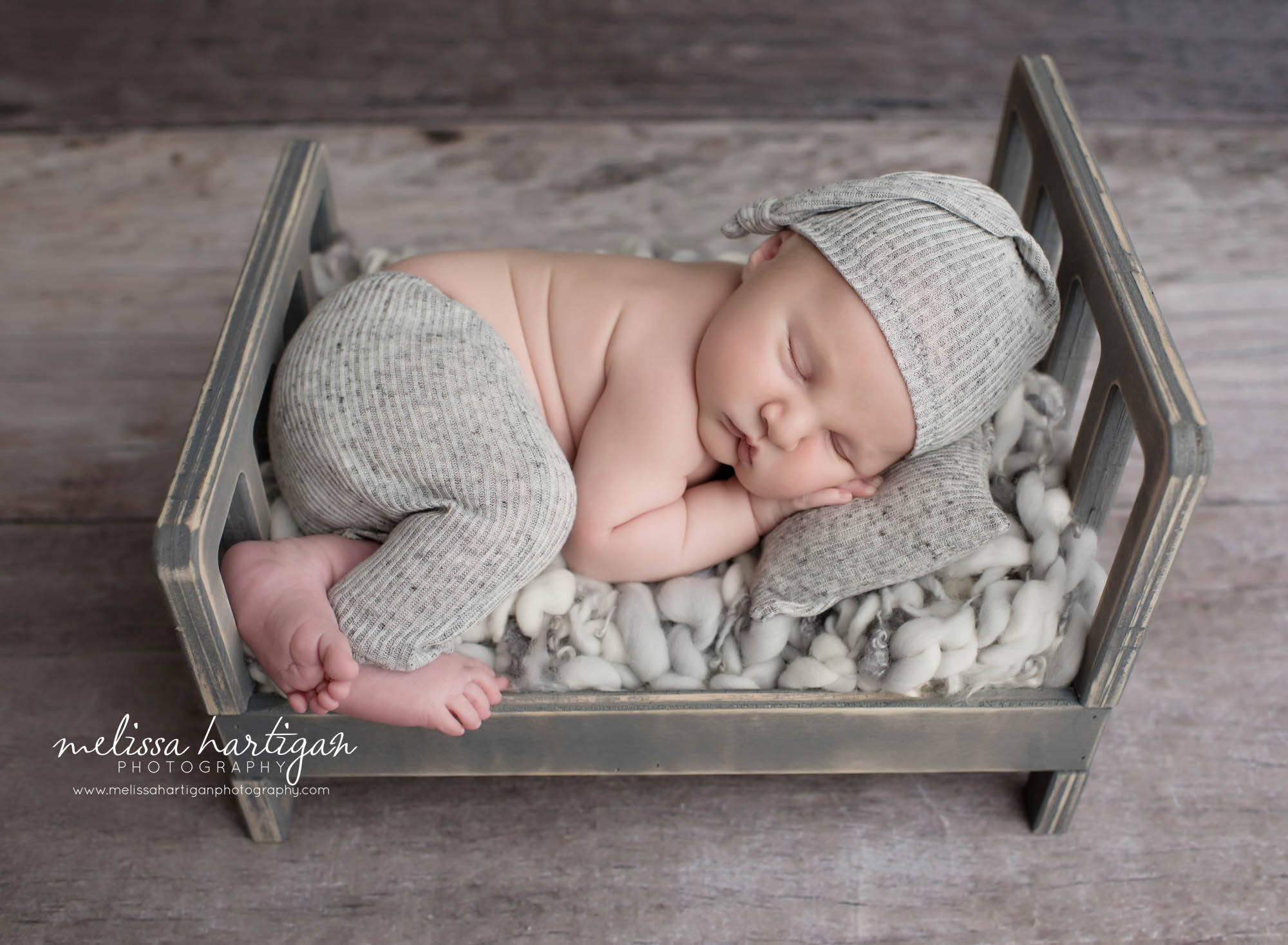 baby boy posed on wooden bed prop wearing gray pants and hat set