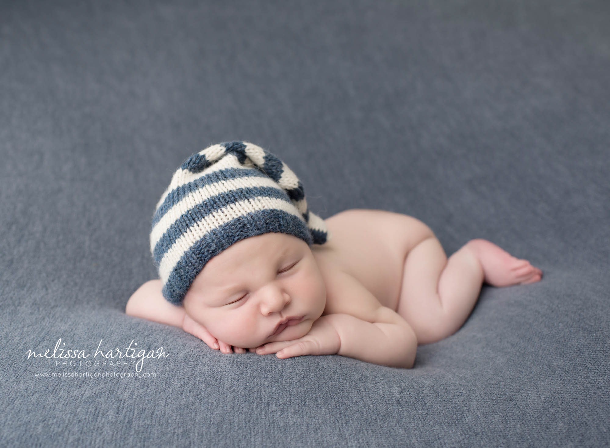 baby boy posed on tummy with hand under cheek and chin wearing striped cream and blue knitted hat