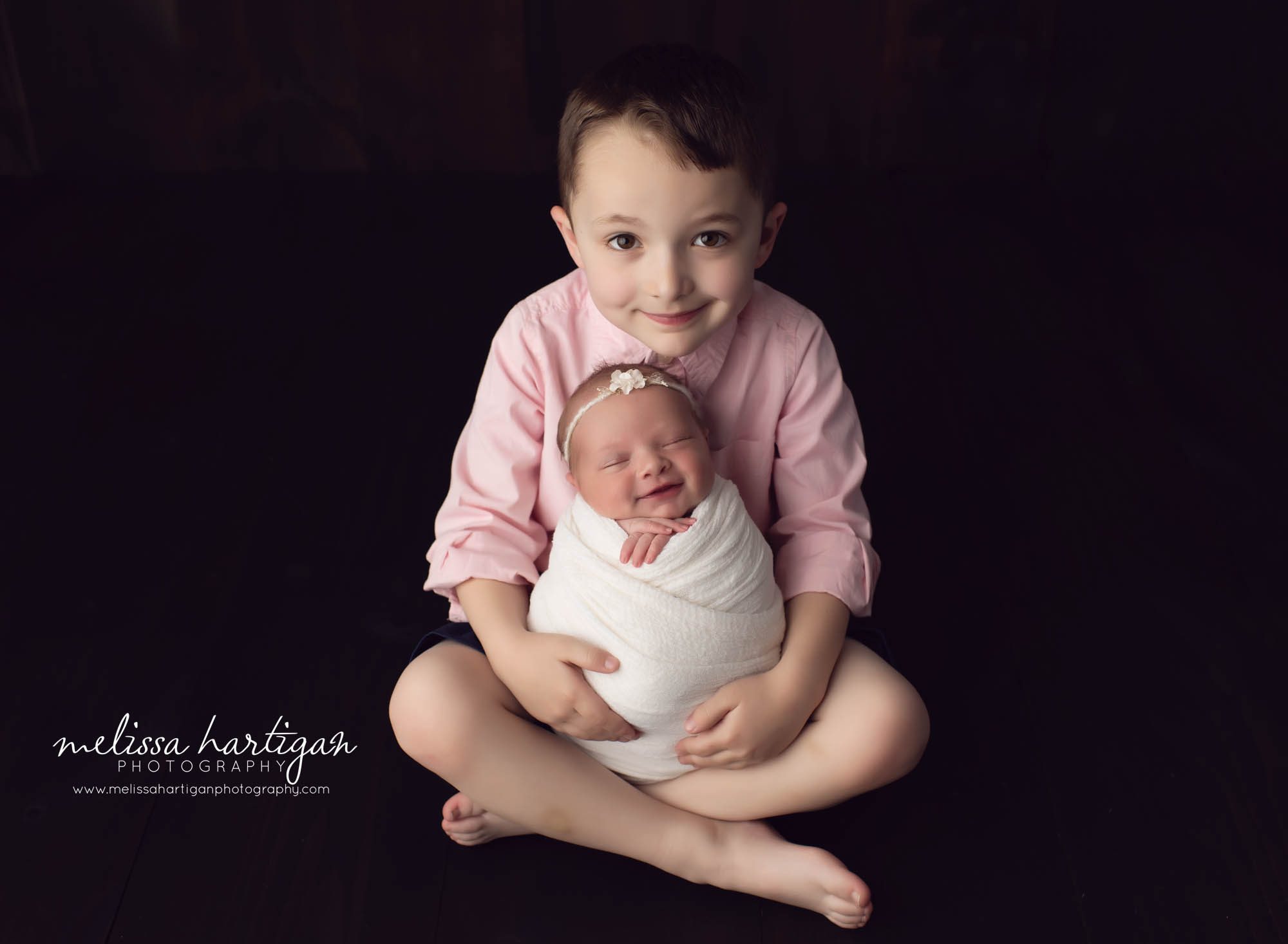 older brother sitting down holding baby sister in studio newborn photography session CT baby photographer