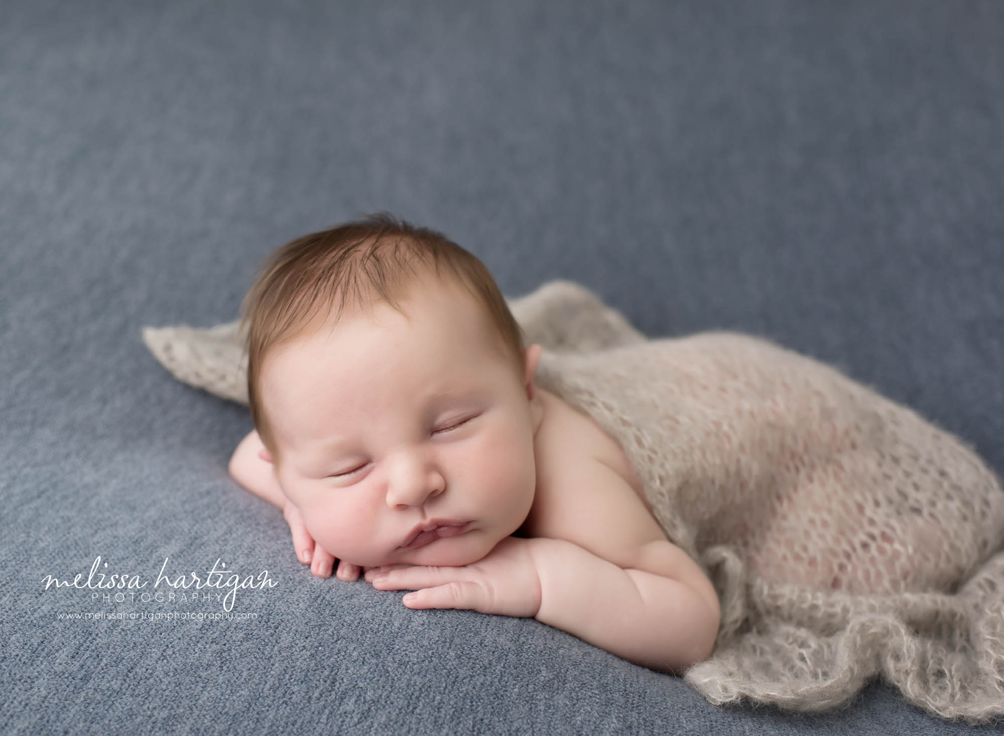 baby posed posed on blue blanket backdrop with light gray knitted wrap