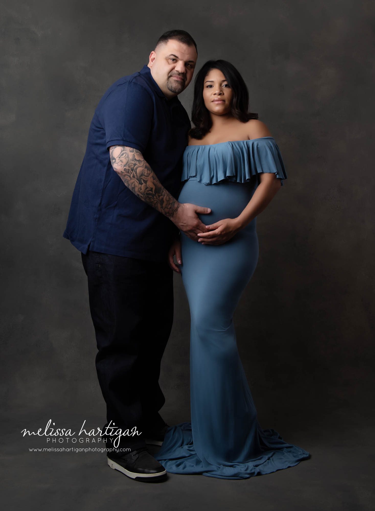 mom and dad standing in maternity session photoshoot holding moms belly wearing blue colors expecting baby boy