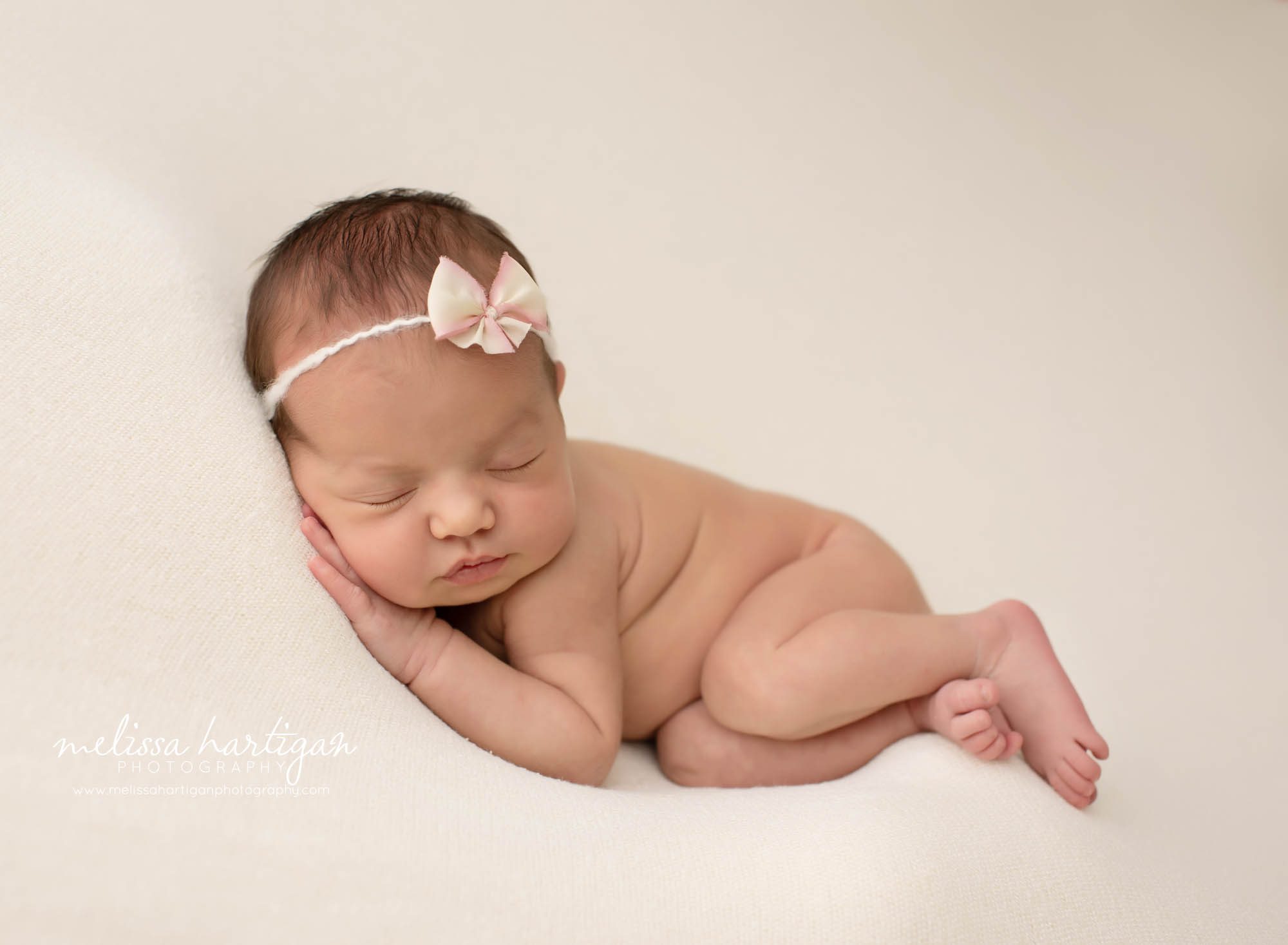 baby girl posed on cream colored blanket with pink and cream bow tie back