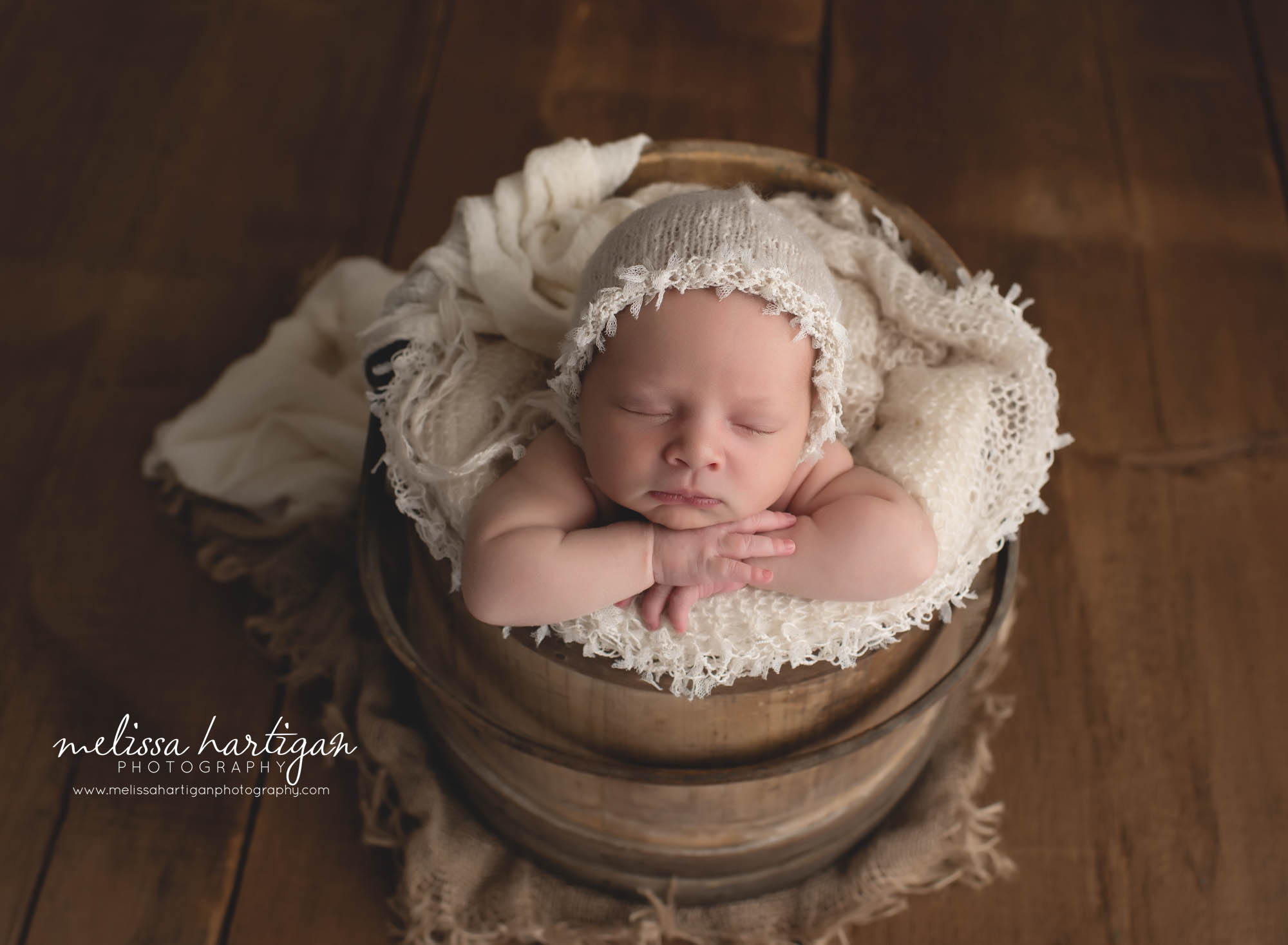 baby girl posed in wooden rustic bucket with cream fringed bonnet