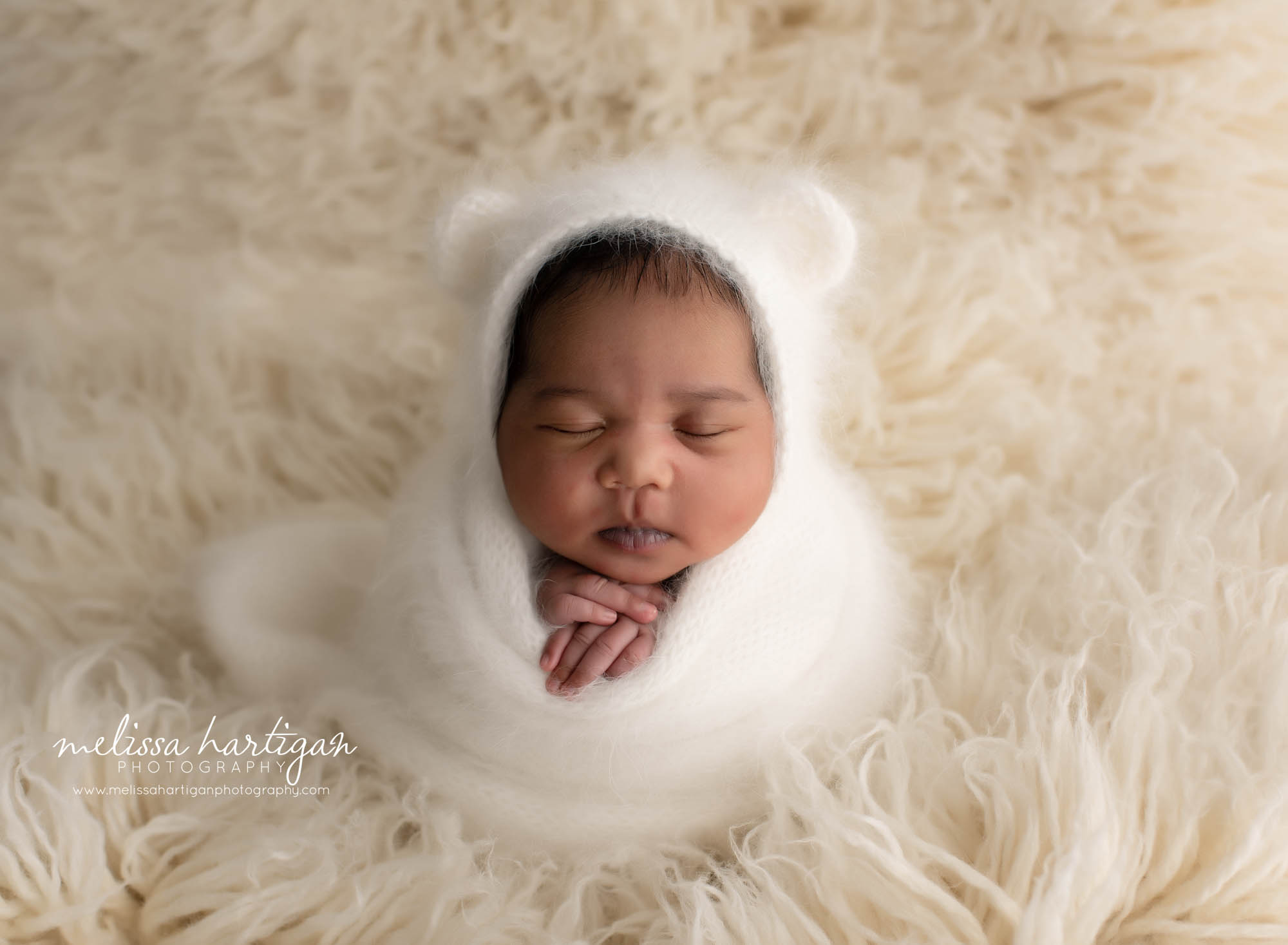 baby girl posed on cream colored flokati with white knitted bear bonnet and wrap