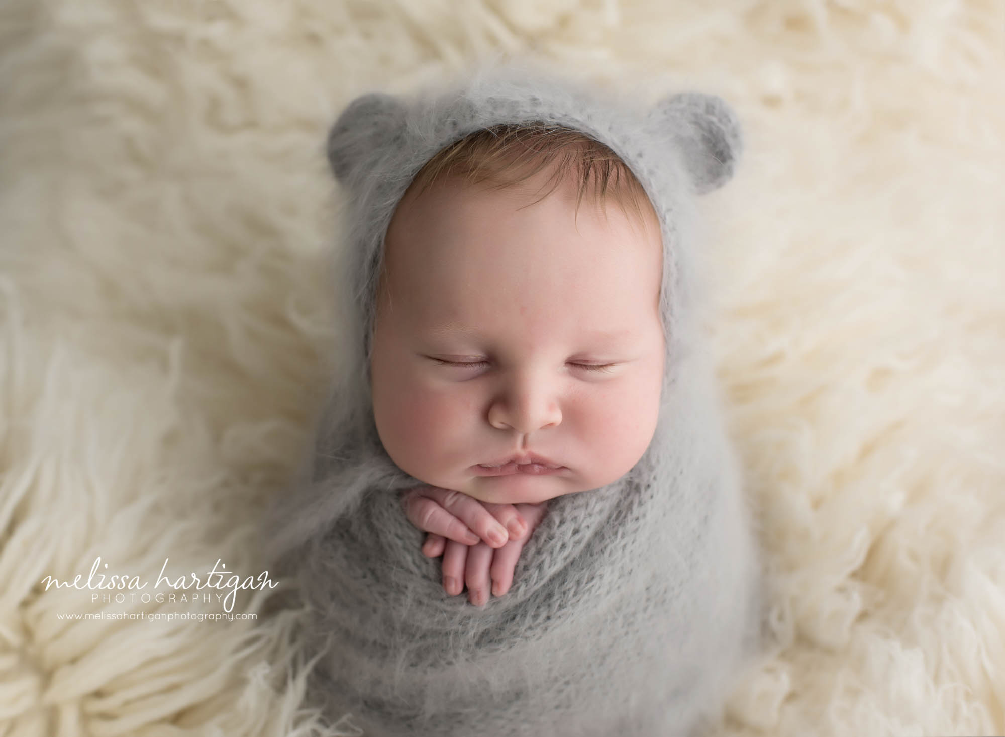 baby boy wrapped in gray wrap and gray bear bonnet on flokati
