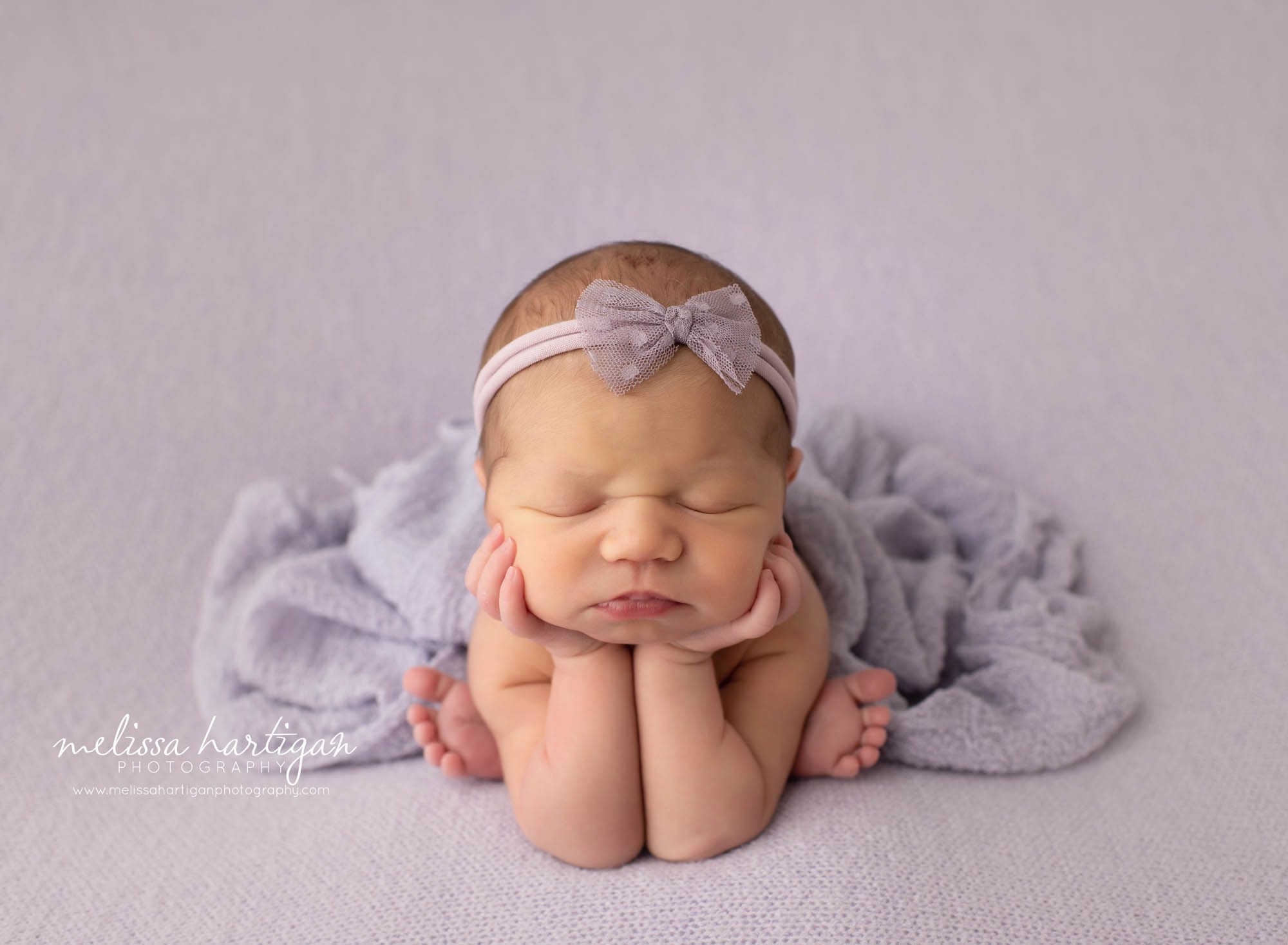 Baby girl posed in froggy pose on purple backdrop with purple bow headband