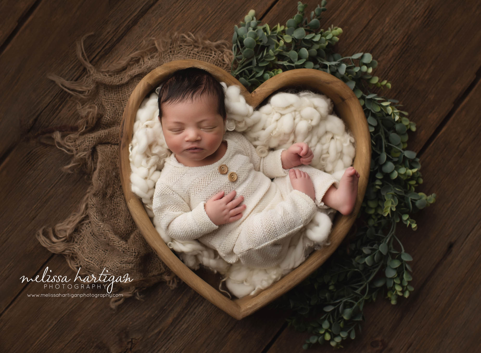 Baby boy wearing cream newborn outfit posed in wooden heart prop