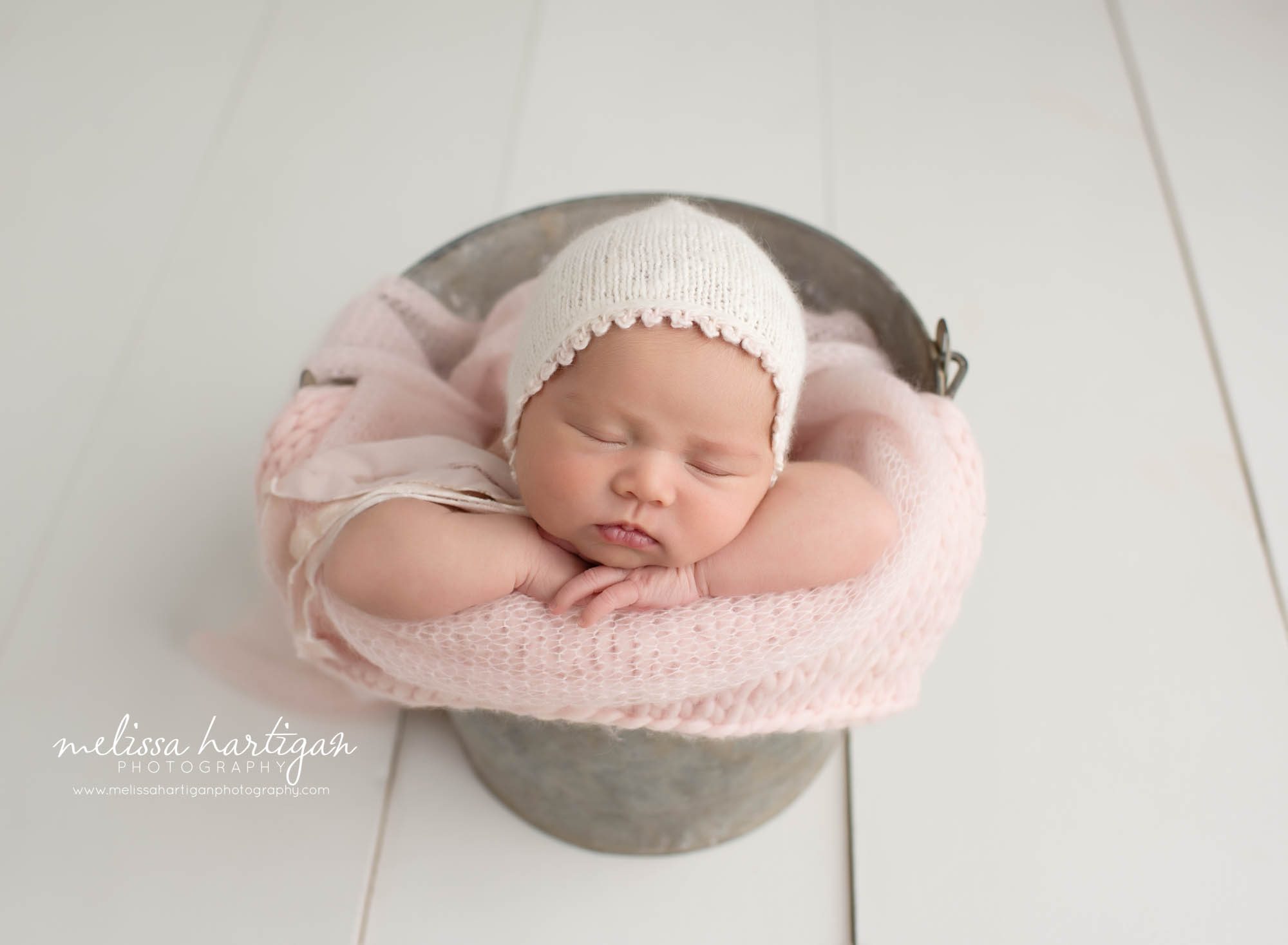 baby girl posed in metal bucket with baby pink knitted bonnet and layer wrap