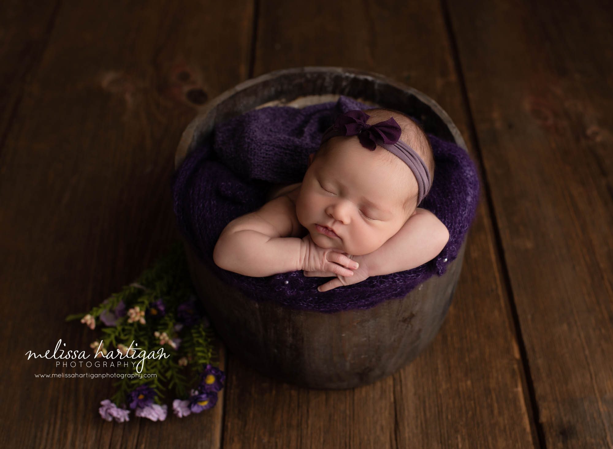 baby girl posed in bucket with purple flowers and purle bow headband