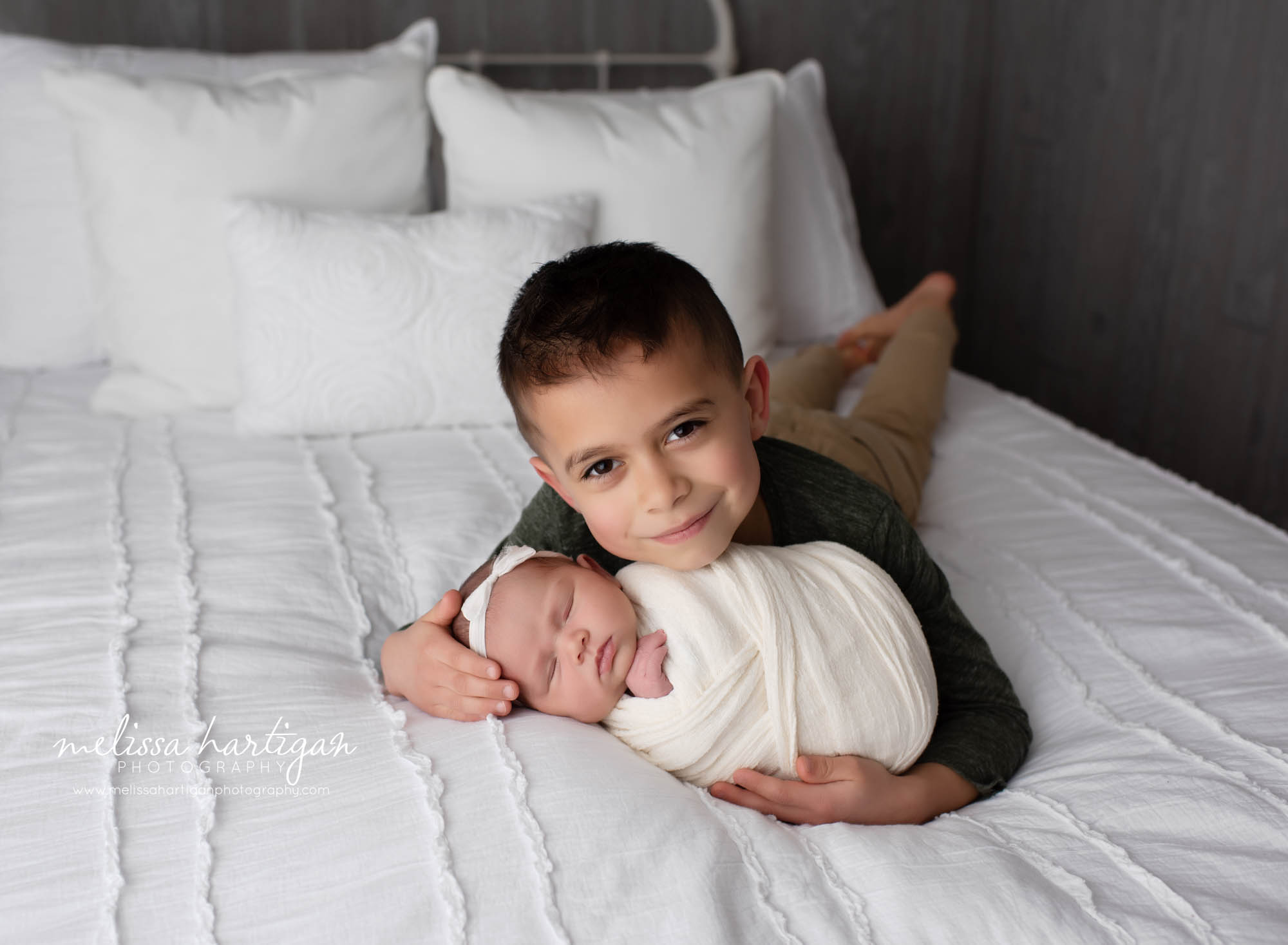 Older brother holding newborn baby sister on bed in studio session