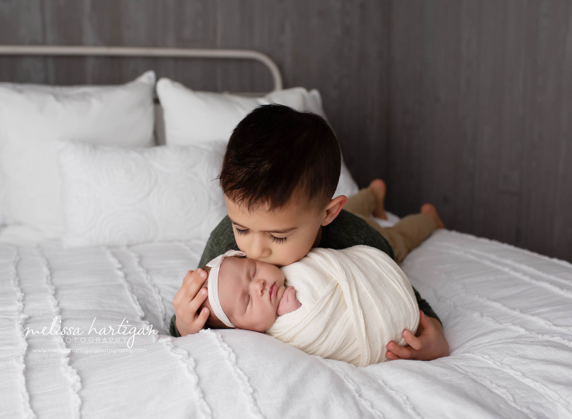 older brother giving new baby sister a kiss on the cheek studio newborn photography session CT