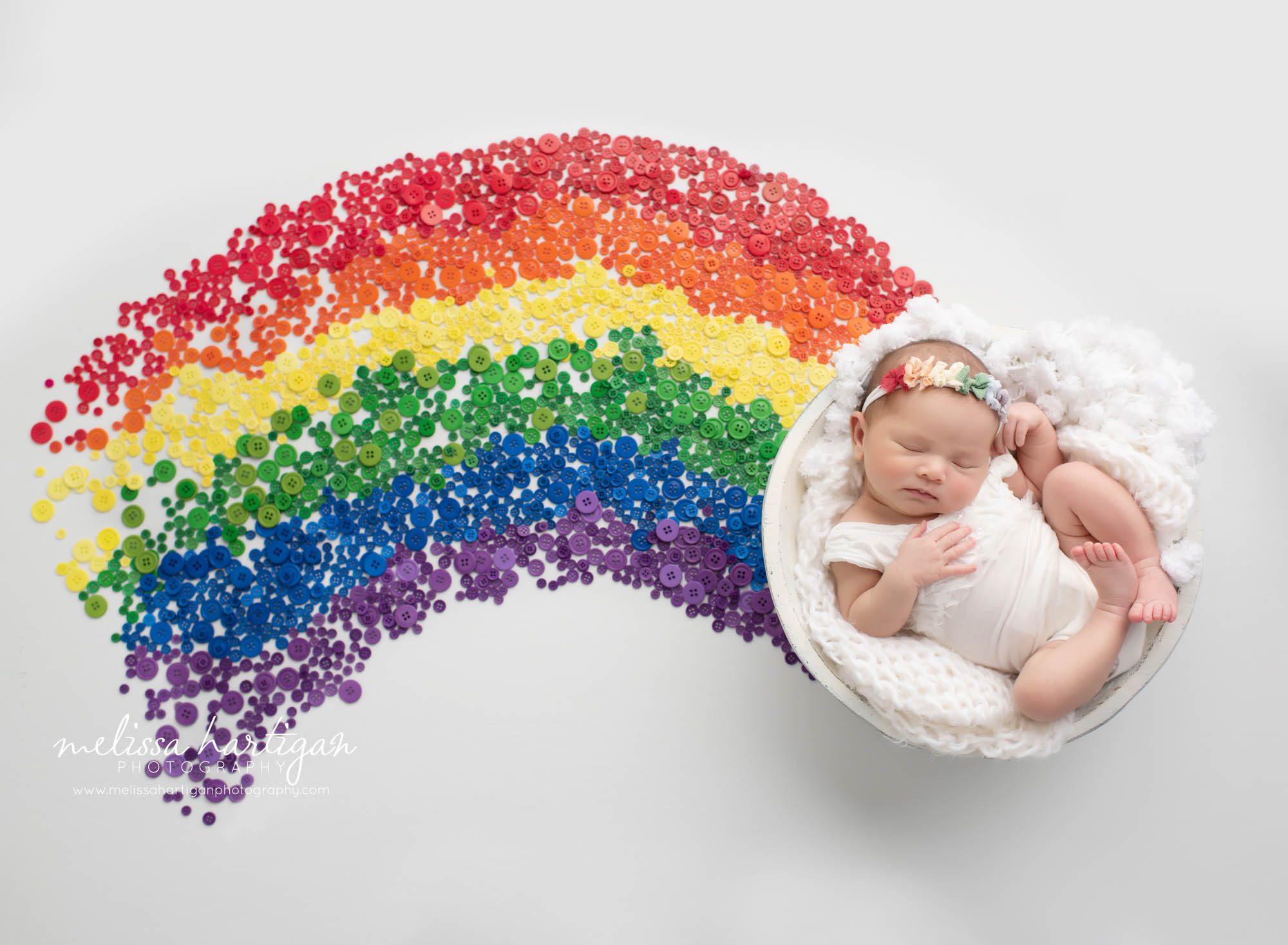 baby girl posed in wooden bowl wearing rainbow colored headband and 10552 button in the color of the rainbow to signify what a rainbow baby is CT newborn Photography