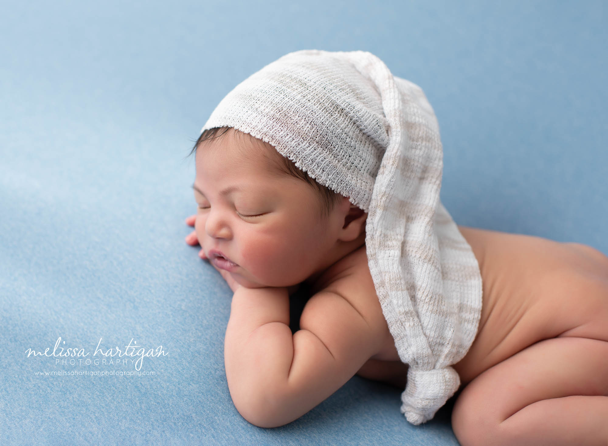 Baby boy posed on blue blankte wearing cream colored sleepy cap