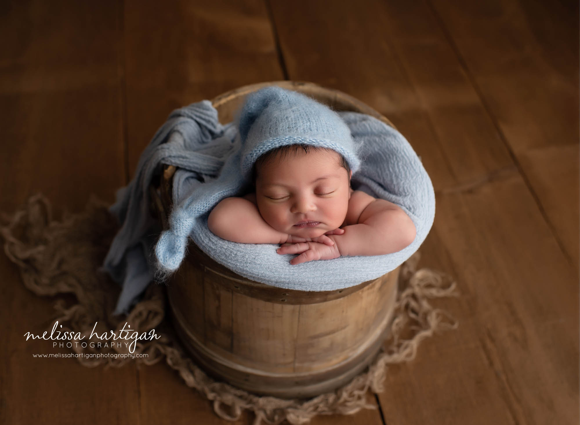 Baby boy posed in rustic wooden bucket with light blue kitted sleepy cap and wrap