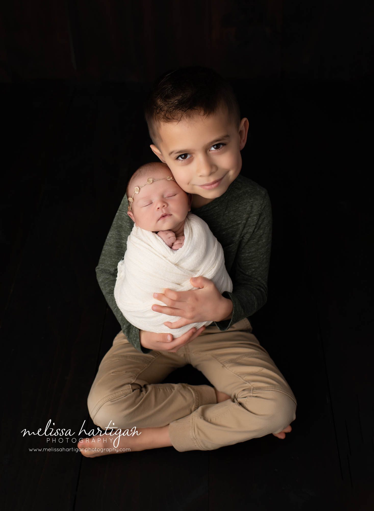 big brother holding new baby sister sitting cross legged in studio newborn photography session