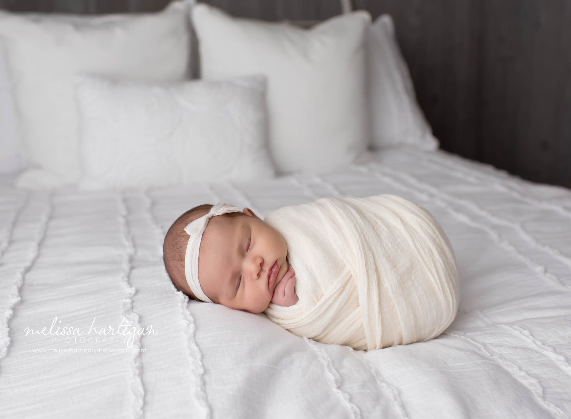 baby girl wrapped in cream wrap on bed wearing cream bow headband