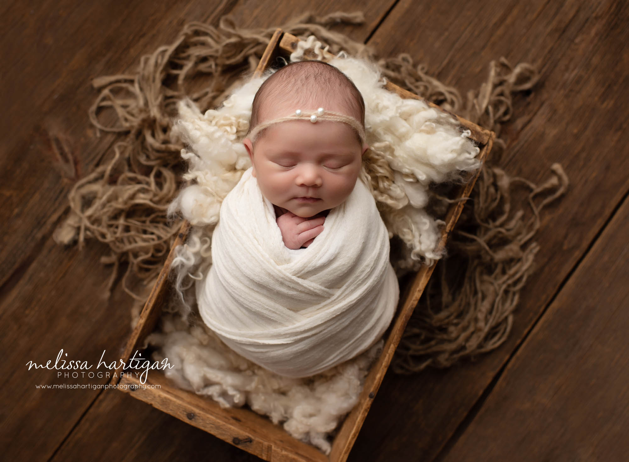 baby girl posed on back with cream colored wrap in wooden crate